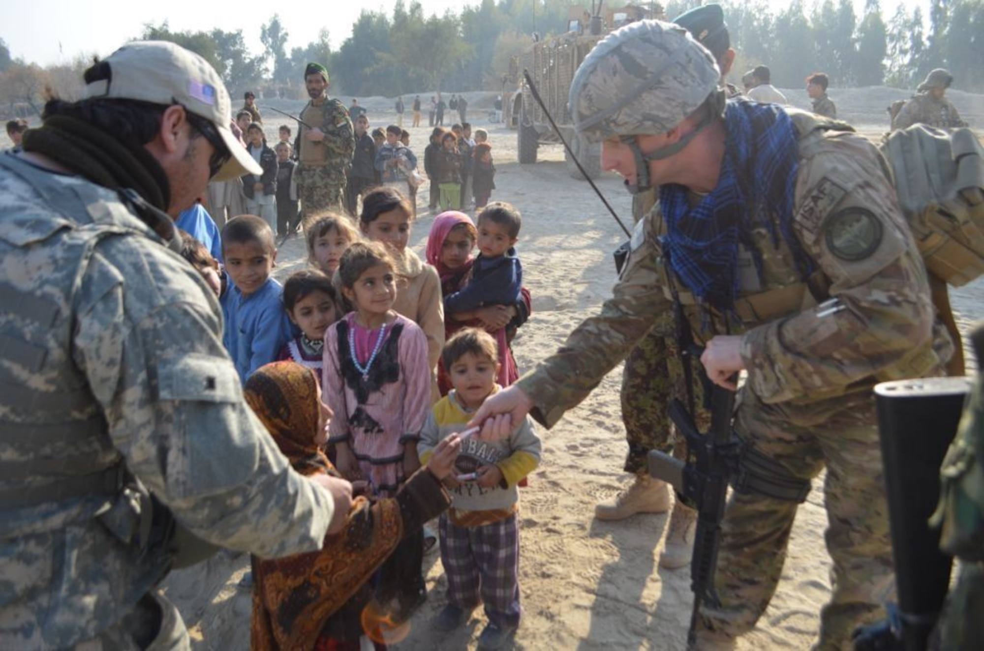 An Afghan child accepts a gift of school supplies from Lt. Col. Jason Wollard, Commander of Detachment 1, 438th Air Expeditionary Advisory Group, near Jalalabad, Afghanistan, Dec. 25. The 438th AEAG team, based at Kabul, Afghanistan, was on a security mission with the U.S. Army and members of the Afghan Air Force when they stopped to distribute school supplies donated by families of U.S. Army personnel and members of the 438th AEAG to two tribal maliks, or chieftains, and the headmaster of a local school. Wollard is deployed from the Safety  directorate at Air Force Global Strike Command, Barksdale Air Force Base, La. (U.S. Army photo by Specialist Erika Clarkson)
