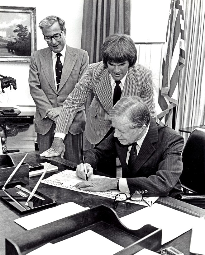 President Jimmy Carter signs up for the monthly purchase of a savings bond in the White House Oval Office, April 9, 1980. Defense Secretary Harold Brown, left, served as chairman of the government-wide Savings Bond campaign, and baseball star Pete Rose, center, was the honorary chairman.  