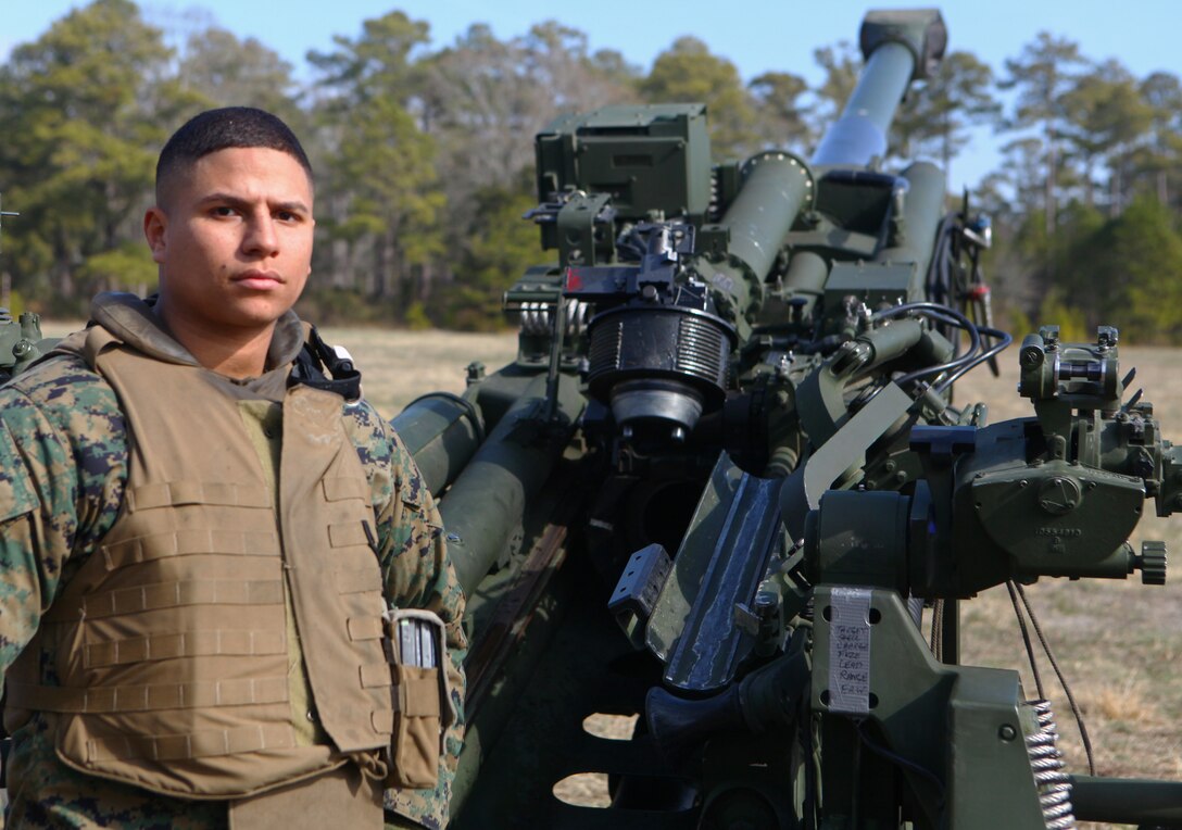 Corporal Eduardo Munoz, an assistant section chief and gunner with Romeo Battery, 5th Battalion, 10th Marine Regiment, 2nd Marine Division, stands next to an M777 Howitzer.  Munoz enlisted in the Marine Corps three years ago and has been shooting artillery for a year.