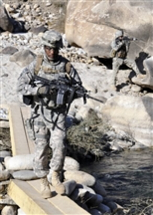 U.S. Navy Petty Officer 1st Class Brylan Riggins (left), with the Nuristan Provincial Reconstruction Team, crosses a temporary bridge on the Alingar River as U.S. Army 1st Lt. Michael Lutkevich, Nuristan Provincial Reconstruction Team security force platoon leader, stands guard in Nuristan province, Afghanistan, on Jan. 23, 2011.  The Provincial Reconstruction Team and the United States Agency for International Development checked on the status of a watershed project designed to mitigate the effects of unchecked soil erosion.  