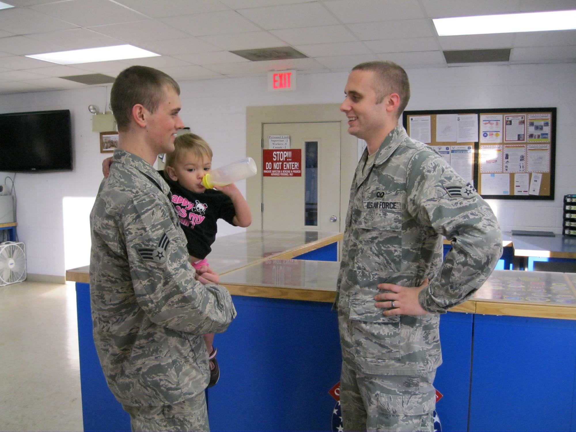 SEYMOUR JOHNSON AIR FORCE BASE, N.C. - Senior Airman Colton Brown holds his daughter as he talks to his friend, Senior Airman Erving Perkins at the parachute building here, Jan. 28, 2010. While deployed to Joint Base Balad, Iraq, in September 2010, Airman Brown developed a very rare condition causing fluid to surround his heart and lungs. He was medically evacuated to Walter Reed Army Medical Center, Md., where Airman Perkins was stood by his side until he his discharge. Airman Brown plans to return to full duty in mid-February. Both Airmen are aircrew flight equipment technicians with the 4th Operations Support Squadron. Airman Brown hails from Hampton, Ohio, and Airman Perkins is from Beacon, N.Y. (U.S. Air Force photo/Senior Airman Marissa Tucker)