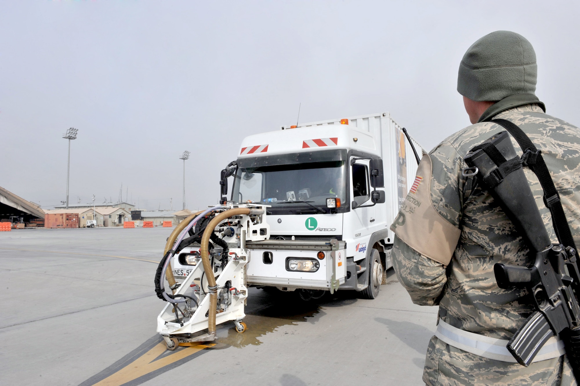 Senior Airman Robert Harris watches a contractor from EMTA Electric Engineering Construction Contracting and Trade Inc. remove paint Feb. 1, 2011, at Bagram Air Field, Afghanistan. EMTA, a company headquartered in Turkey, has been contracted to remove excess rubber from runways and repaint more than 40 aircraft parking spaces here. Airman Harris is a force-protection escort assigned to the 455th Expeditionary Civil Engineer Squadron. (U.S. Air Force photo/Senior Airman Sheila deVera) 