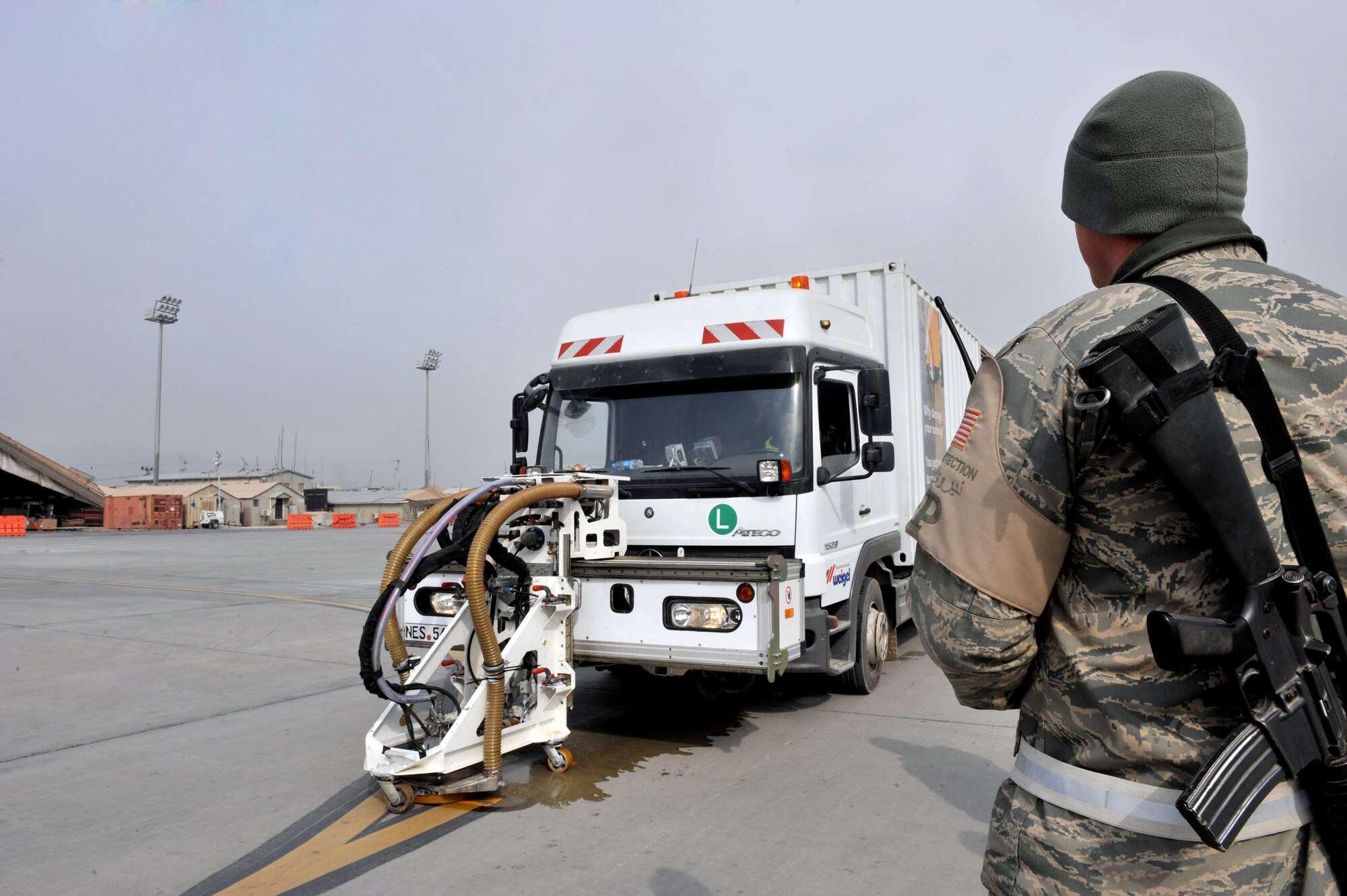 Senior Airman Robert Harris, 455th Expeditionary Civil Engineer Squadron force protection escort, watches an EMTA contractor remove paint at Bagram Air Field, Afghanistan, Feb. 1, 2011. EMTA, a company headquartered in Turkey, has been awarded to remove excess rubber from runway and repainting of more than 40 aircraft parking spaces. Airman Harris is deployed from the 388th Combat Training Squadron, Offut Air Force Base, Neb. (Air Force photo by Senior Airman Sheila deVera)