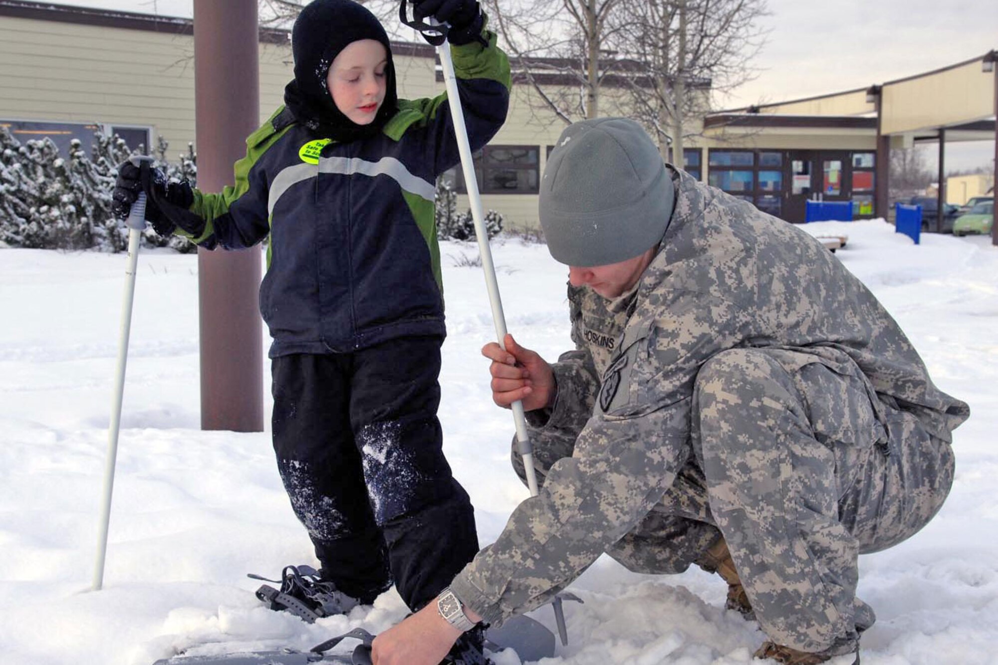 Army Chaplain (Capt.) Logan McCurdy of 2nd Battalion, 377th Parachute Field Artillery Regiment, 4th Brigade Combat Team (Airborne), 25th Infantry Division, helps a student from Orion Elementary School into a pair of snowshoes, Jan. 21, during a demonstration of Army equipment as part of a partnership program with the Anchorage School District allowing for service members to volunteer with various schools. (U.S. Army photo/Sgt. Marcus Butler)