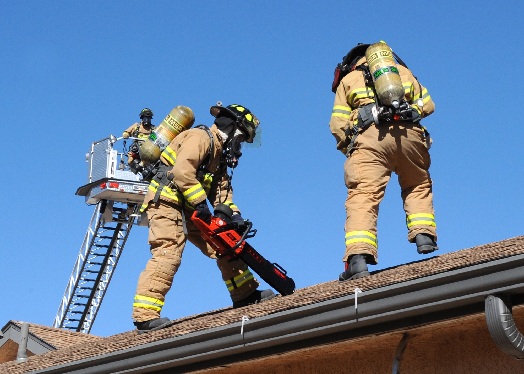 Firemen simulate cutting into the roof of a house to vent fire and smoke.  U.S. Air Force Photo by Dennis Carlson.