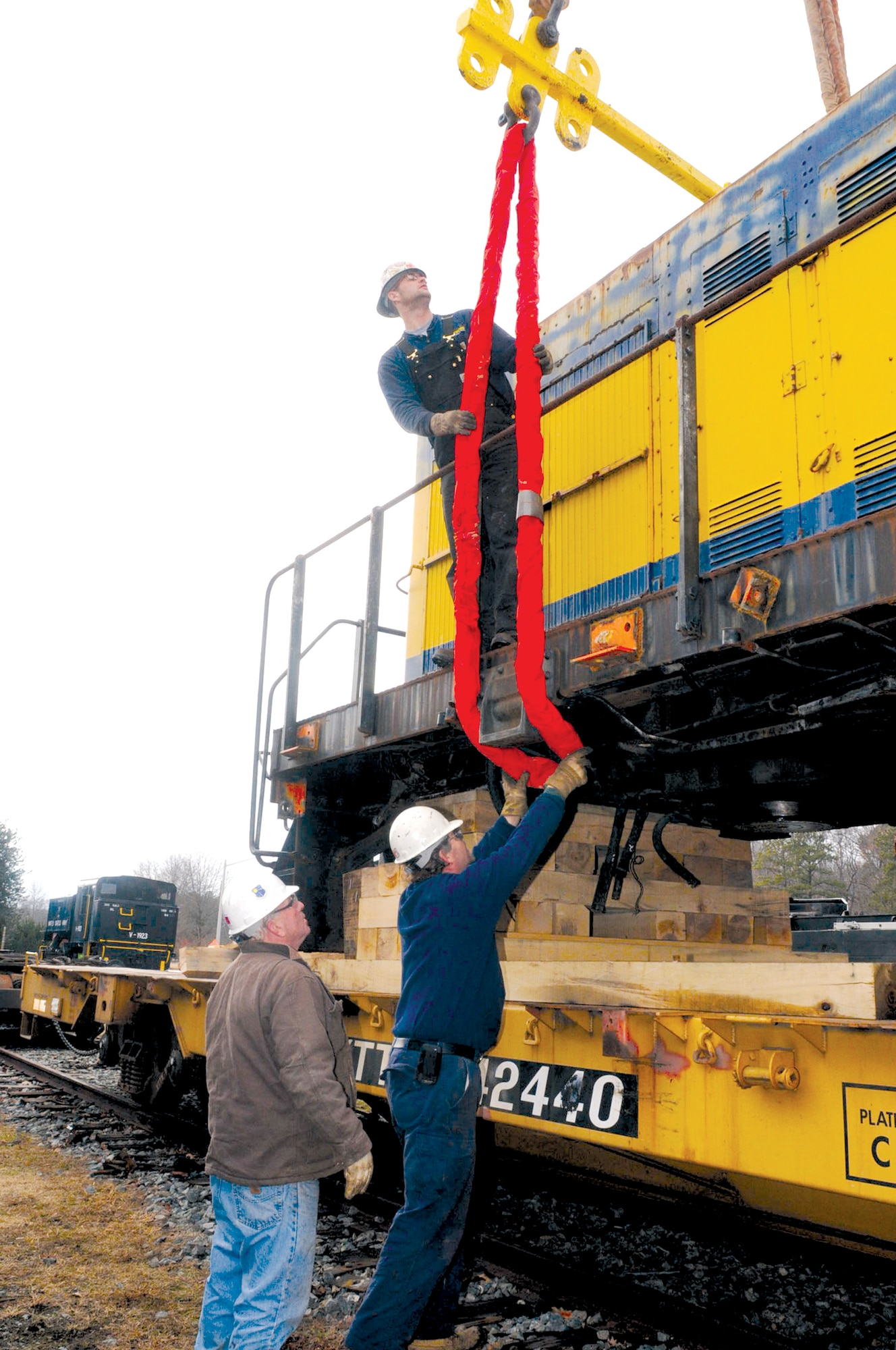 Mike Evans (center), an ironworker with Lockwood Bros., secures a cable onto a loading hook on the underside of the engine in preparation to lift the nearly 75-ton engine from the flatbed car as Daryl Hein (above), an operator apprentice, and Harry Fetter (left), ironworker foreman, look on. (Photo by Lyna Tucker)


