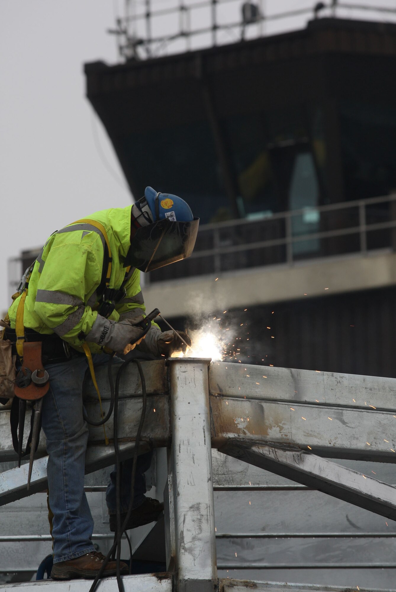 Construction crews weld anchors onto the frame of the new tower cab frame ensuring a secure hold prior to lifting it into its place at the top of the control tower main structure Jan 31. (U.S. Air Force Photo/Don Peek)