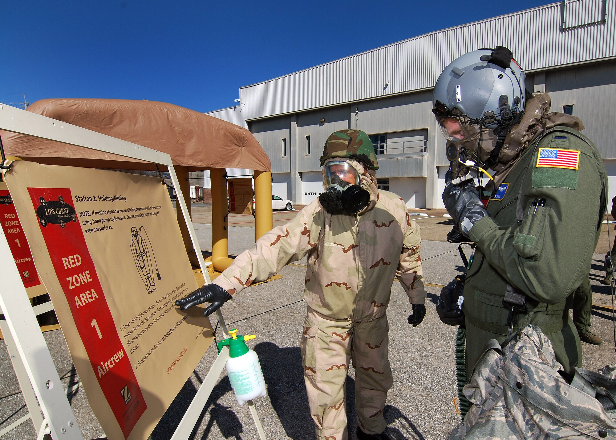 Tech Sgt. Lance Wilson, an Aircrew Flight Equipment technician, briefs 1st Lt. Seth King on the decontamination procedures at this spray down station, Feb 6.  A lucky couple of airmen get to dress out and go through the stations as the rest of the class observes for the refamiliarization training.  The training takes them from start to finish through an Air Force decontamination line and provides good insight as to what to they will experience in the process.  (U.S.  Air Force photo/ Brad Fallin)