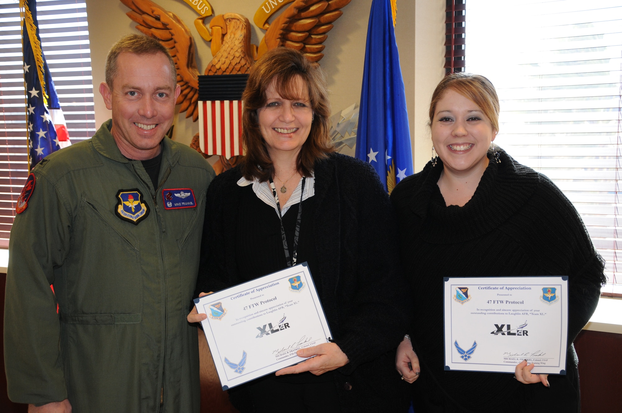 LAUGHLIN AIR FORCE BASE, Texas – Michele Perez and Kim Vaughn, both of 47th Flying Training Wing Protocol, pose with Col. Michael Frankel, 47th FTW commander, after being presented the XLer of the Week award Feb. 9. The XLer is a weekly award chosen by wing leadership and given to those who consistently make outstanding contributions to Laughlin and their unit. (U.S. Air Force photo by Airman 1st Class Blake Mize)