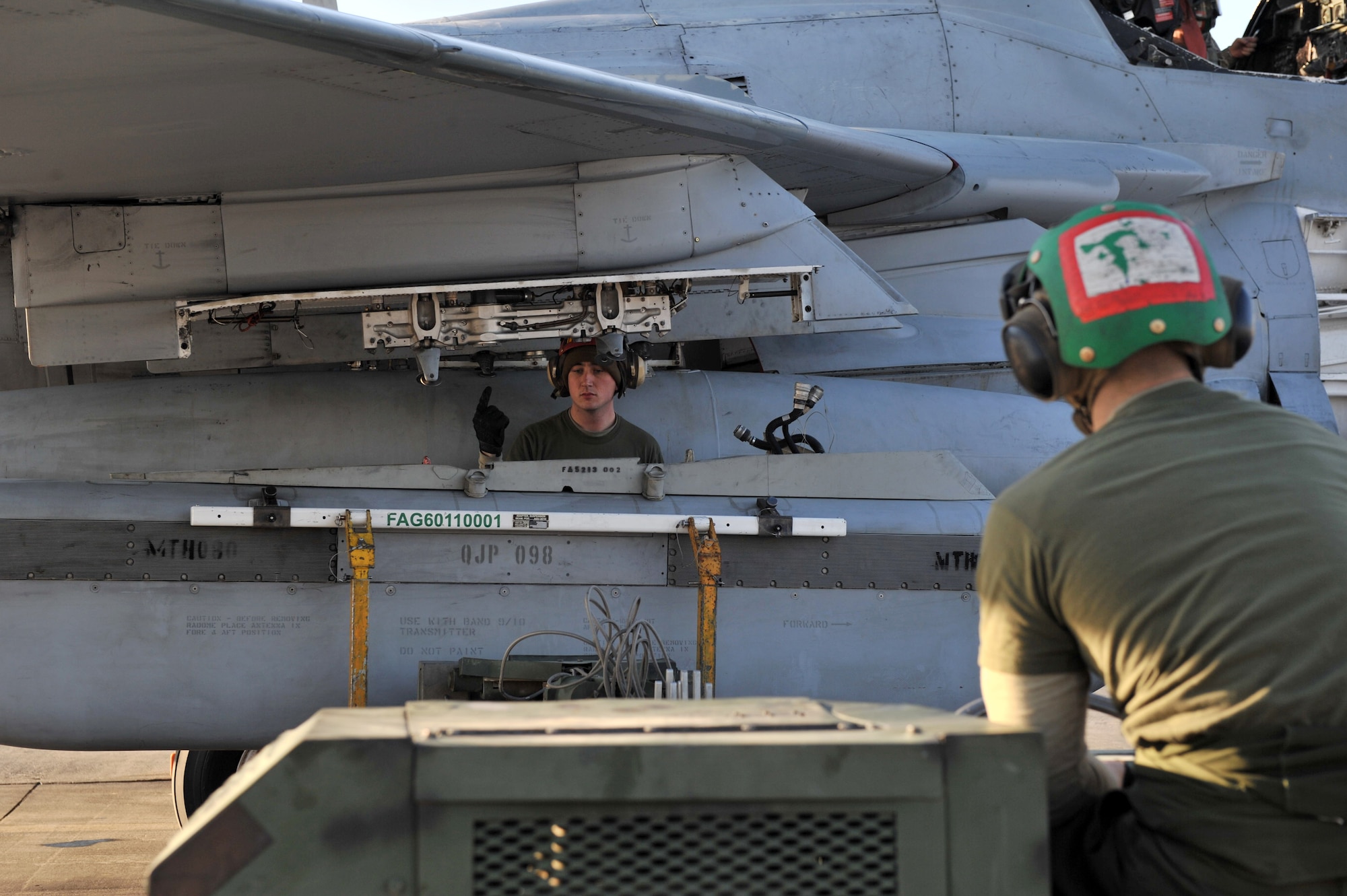 Lance Cpl. Edward Helmick an aviation ordnance technician, guides Lance Cpl. Robert Starmer an electronic countermeasure technician, while installing an ALQ-99 Tactical Jamming System on an EA-6B Prowler electronic warfare aircraft, Bagram Airfield, Afghanistan, Feb. 8, 2011. Corporals Helmick and Starmer are assigned to Marine Tactical Electronic Warfare Squadron 3. (Air Force photo by Senior Airman Sheila deVera)