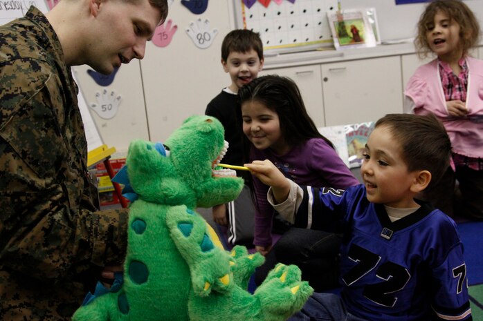 Lt. Edward Wikle, a 3rd Dental Battalion, 11th Dental Company Detachment BHC dentist, uses a puppet dinosaur to teach Matthew C. Perry kindergarten students the imporantace of brushing while Markis Burchett, an M.C. Perry kindergartener, brushes his teeth during a dental staff visit to M.C. Perry elementary school, Feb. 9, to raise awareness for National Children’s Dental health month.
