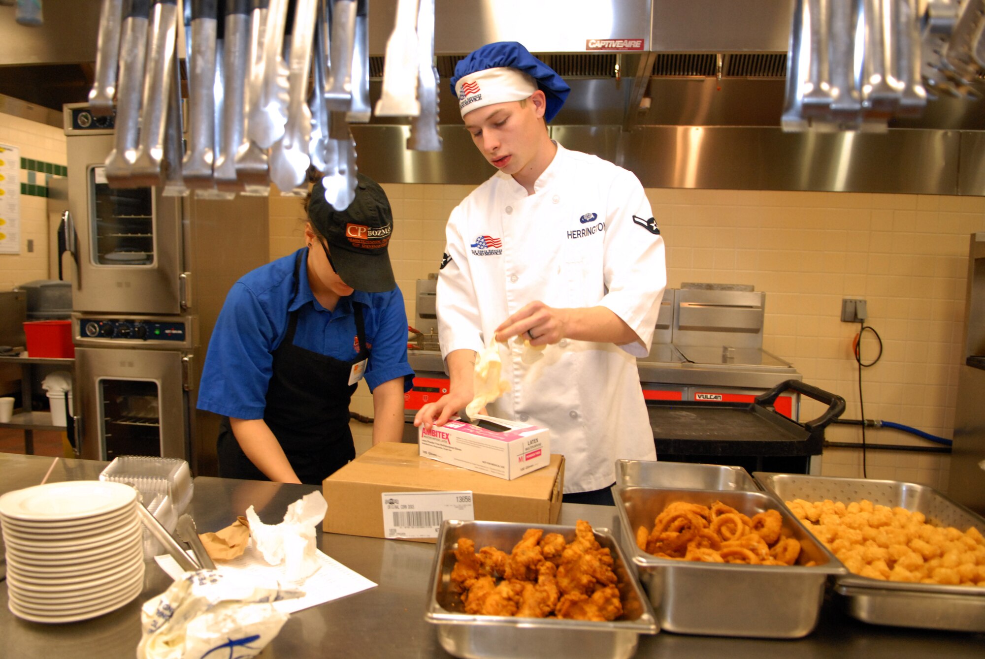 Airman Joshua Herrington, 90th FSS, reaches for gloves prior to handling chicken fingers, onion rings and potato nuggets prepared for the snack line at the Chadwell Dining Facility on F. E. Warren Air Force Base, Wyo. on Jan. 28. (U.S. Air Force photo by R.J. Oriez)