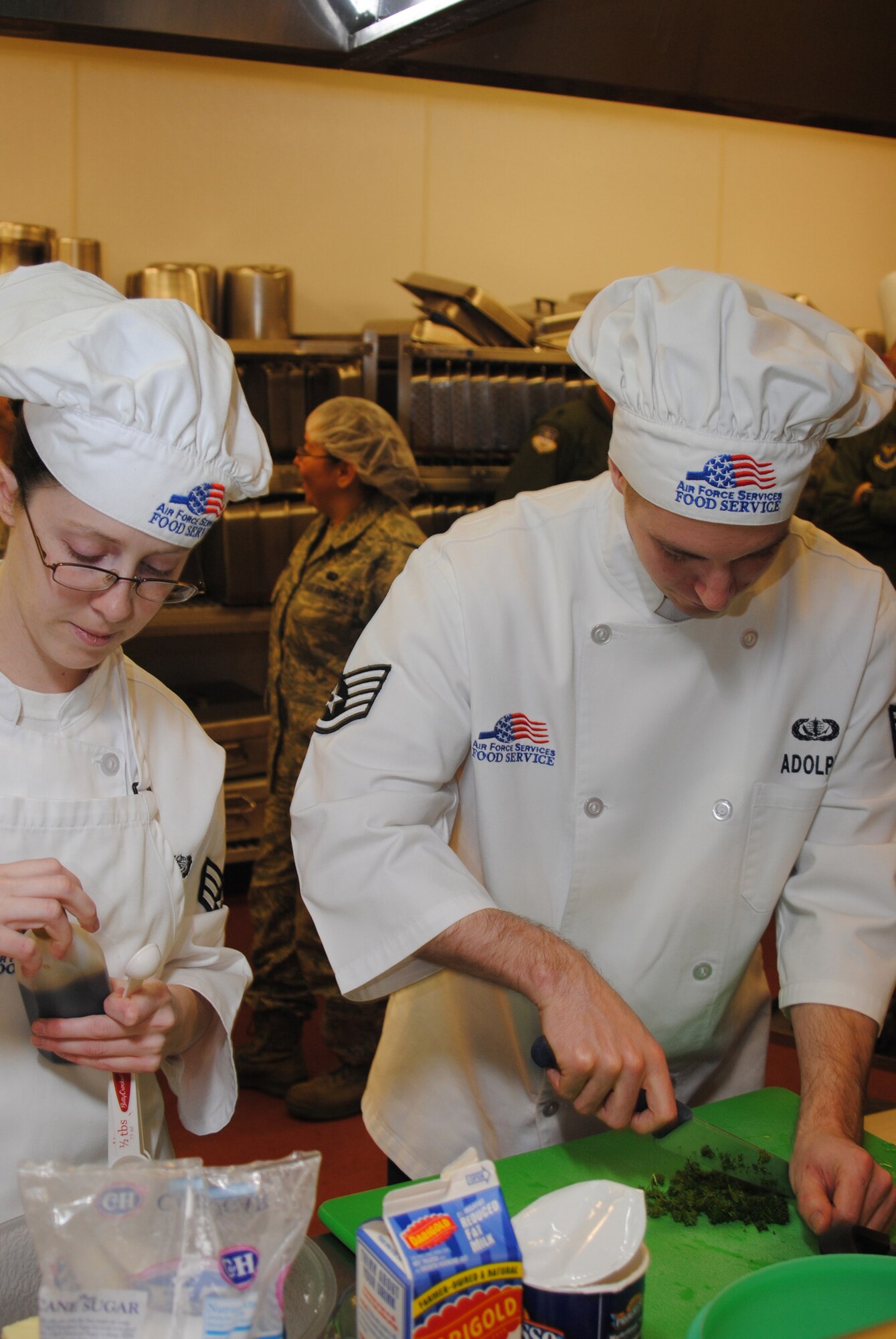Senior Airman Hellen Gisclari  and Staff Sgt. Matthew Adolph, 490th Missile Squadron missile alert facility chefs, work together preparing their meal for the Warrior Chef competition.  They prepared baked pepper jack chicken with fettucini alfredo, and cream cheese-frosted cupcakes for the judges to evaluate. (U.S. Air Force photo/Airman Cortney Hansen)