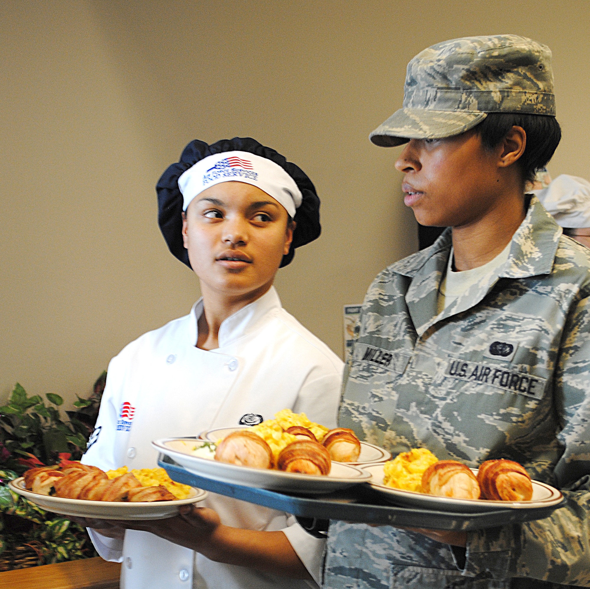 Airman 1st Class Estrella Zapata Miles, 12th Missile Squadron missile chef (left), and Senior Airman Anastasia Miller, also a 12th MS missile chef, wait to serve the judges their meal.  They took the win for the 12th MS with a plate of spinach-stuffed chicken breast and baked macaroni and cheese. (U.S. Air Force photo/Airman Cortney Hansen)