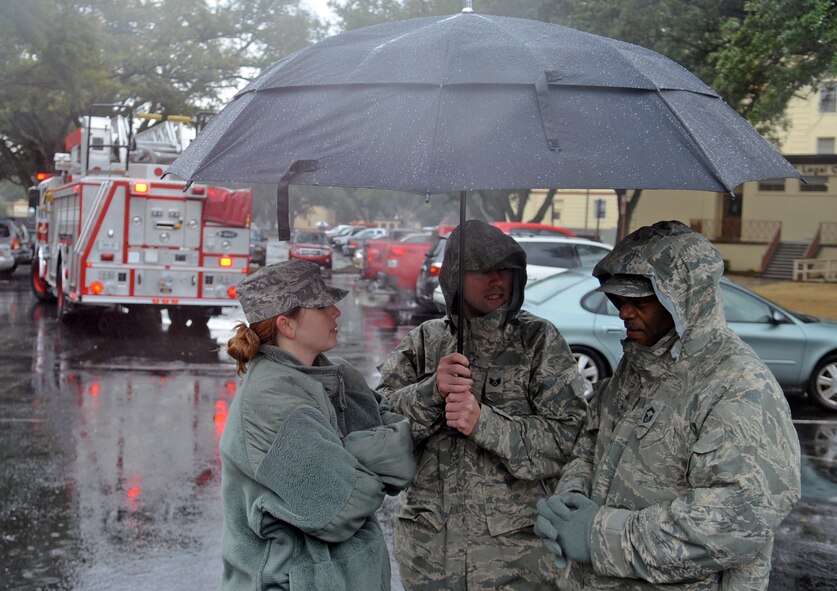 Staff Sgt. Angelique Richardson (left), Staff Sgt. Breihan Fetz (center) and Senior Master Sgt. John Jackson, members of the 2nd Bomb Wing judge advocates office, take shelter under an umbrella during a fire emergency in the parking lot in front of the 2nd Civil Engineer Squadron building on Barksdale Air Force Base, La., Feb. 9. Their building was evacuated for a test of the fire alarm system. (U.S. Air Force photo/Airman 1st Class Micaiah Anthony)