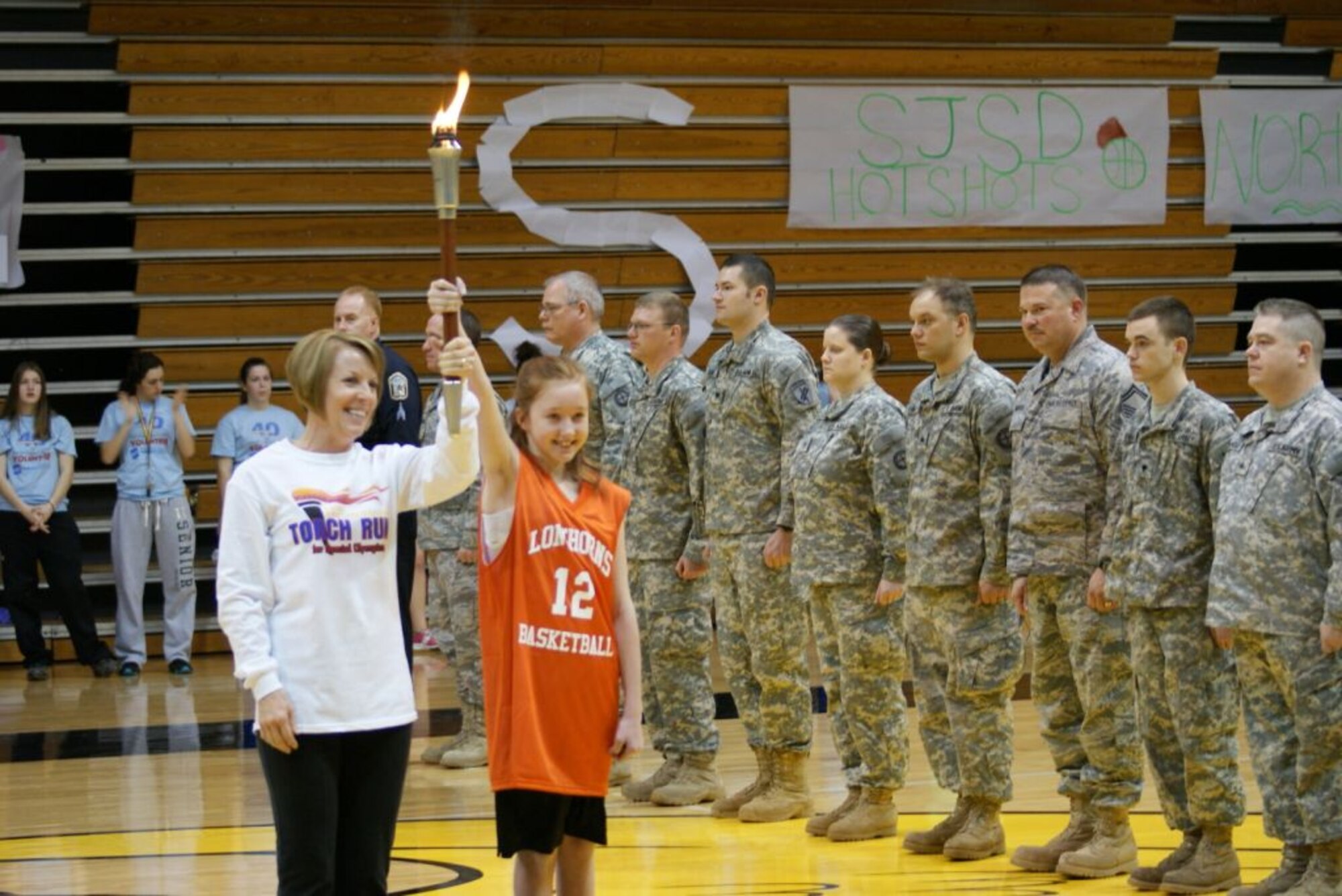 Rita Ketchum (left) and Mysti Lucas (right) brought in the Special Olympics torch during the opening ceremonies of the basketball tournament.  Missouri National Guardsmen, along with other uniformed law enforcement and public safety officers lined the court for the presentation. (Photo by Jennifer Archdekin)