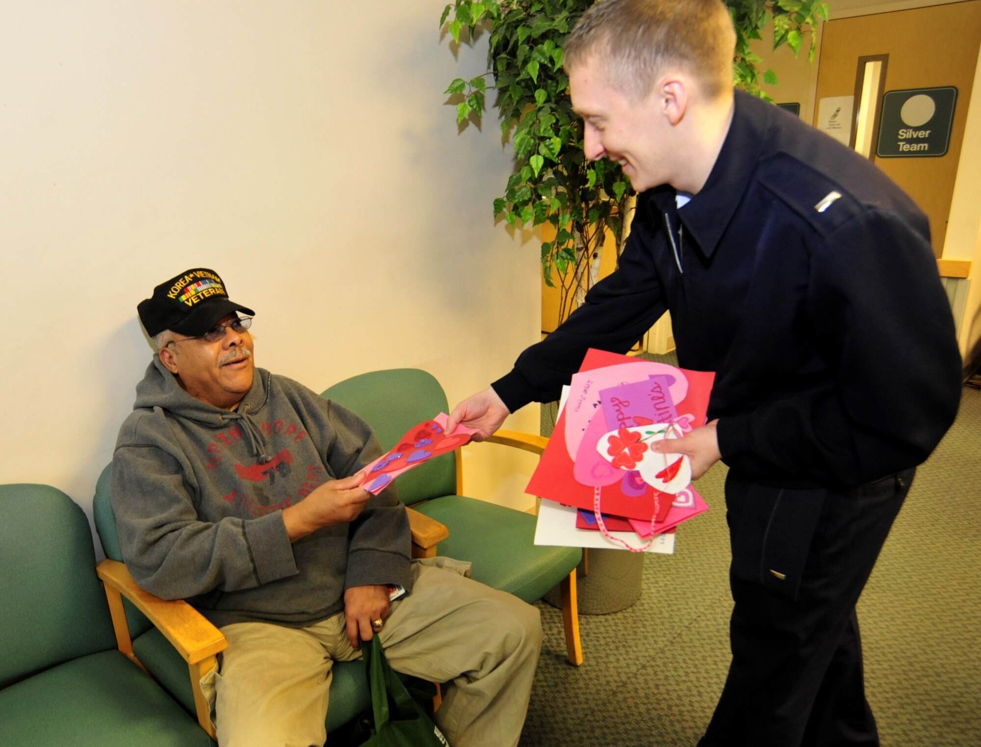 First Lt. Michael Rajchel, right, 627th Logistics Readiness Squadron materiel management flight commander, hands a Valentines’ Day card to Charles Griffin, a United States Army veteran, during a Company Grade Officer Council visit to American Lake veterans' nursing home Feb. 14 in Lakewood, Wash. Eight members of the McChord Field CGOC delivered cards made by second and third grade students at Carter Lake Elementary School. (U.S. Air Force photo/Airman 1st Class Leah Young)