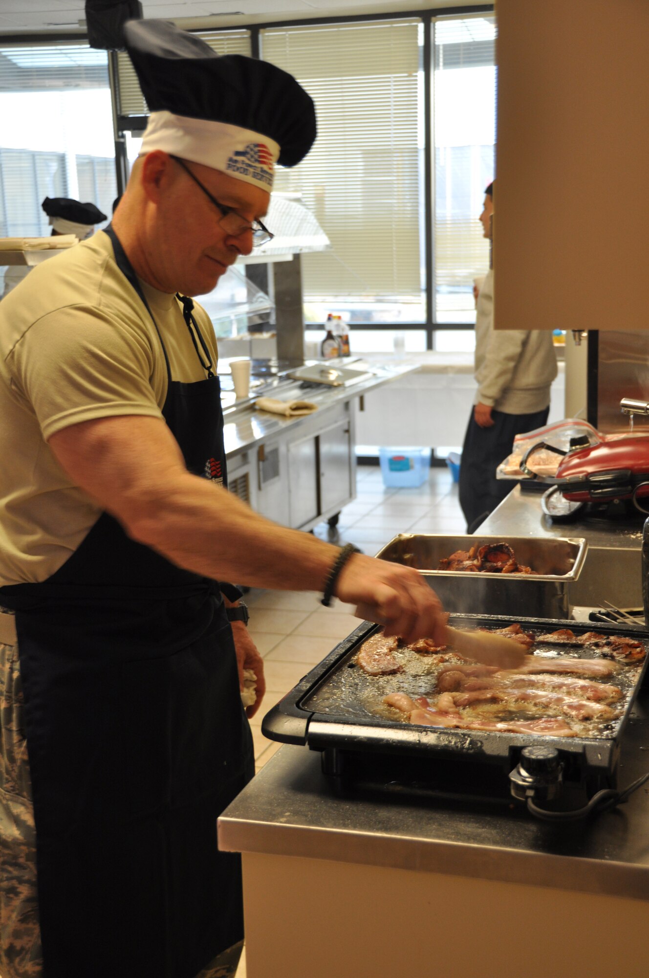 Senior Master Sgt. Mark Lounello, a chaplain's assistant deployed to Air Force Mortuary Affairs Operations, makes some bacon for a breakfast the Top 3 sponsored here Feb. 14, 2011. (U.S. Air Force photo/Christin Michaud)