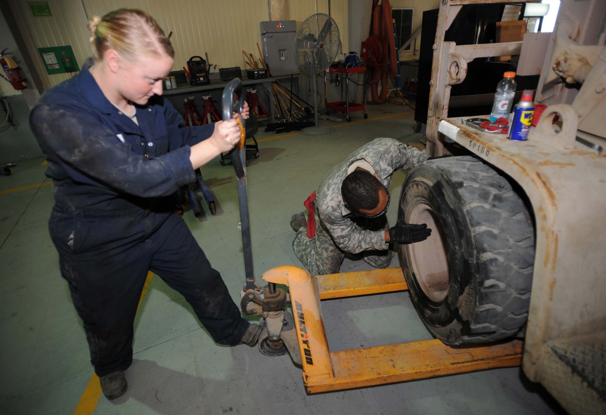 Staff Sgt. Neryssa Adrian assists Senior Airman Brandon Dorsey, both from the 380th Expeditionary Logistics Readiness Squadron, set a forklift tire before reattaching it Jan. 24, 2011, at the vehicle maintenance shop. The shop generally services around three to five vehicles each day. SSgt. Adrian is deployed here from the 133rd LRS, Minnesota Air National Guard. Airman Dorsey is an Air National Guardsman deployed from the 138th LRS, Tulsa AFB, Okla. (U.S. Air Force photo by Senior Airman Maynelinne De La Cruz)