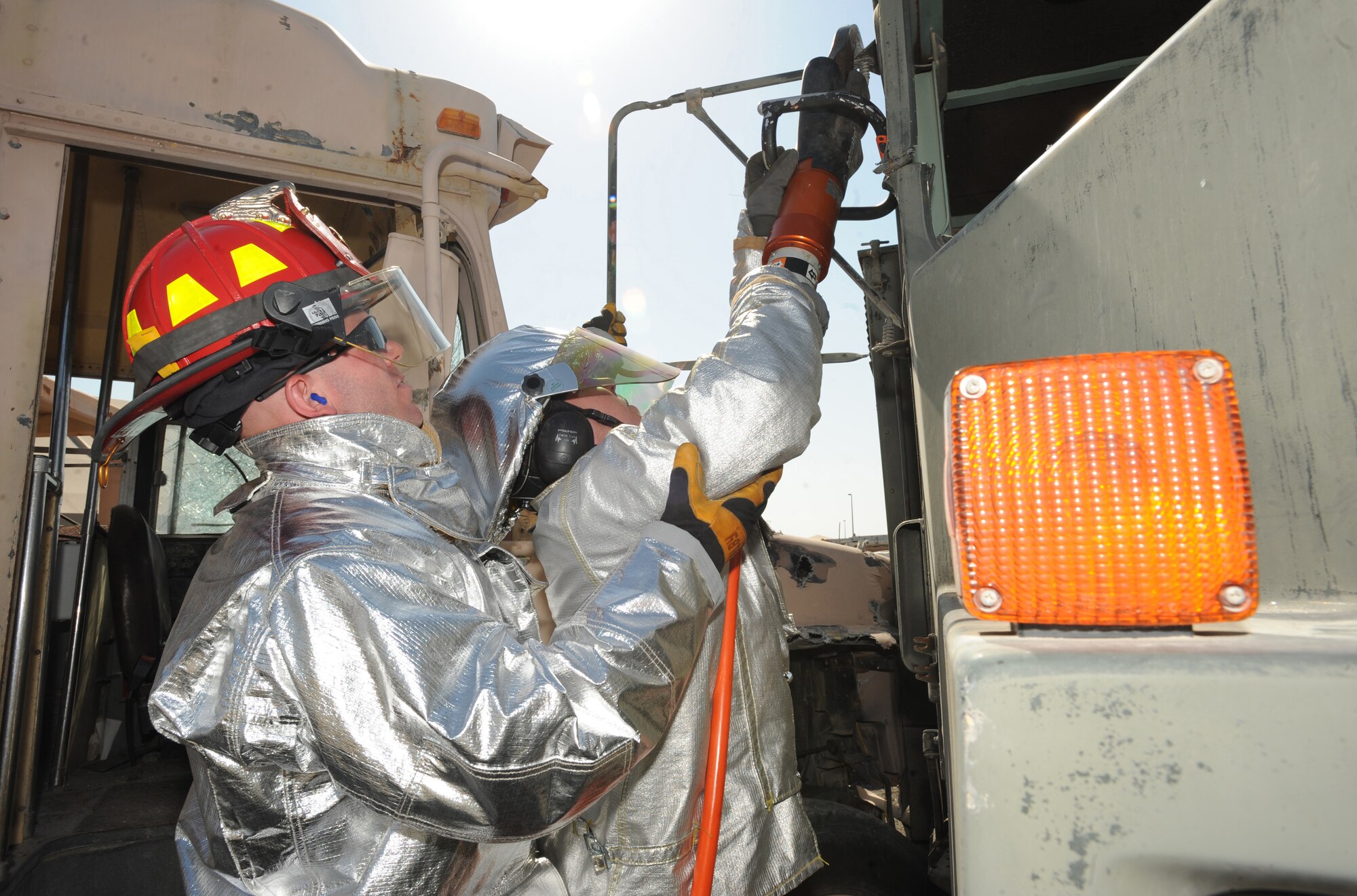 Firefighters from the 380th Expeditionary Civil Engineer Squadron, assist each other in raising a heavy tool called the Jaws of Life enabling them to cut through the truck?s thick steel during an Auto Extrication Exercise on Jan. 28, 2011. These exercises keep the Airmen updated in their training which produce quick decision-making responses and save lives during real world scenarios. (U.S Air Force photo by Senior Airman Maynelinne De La Cruz)