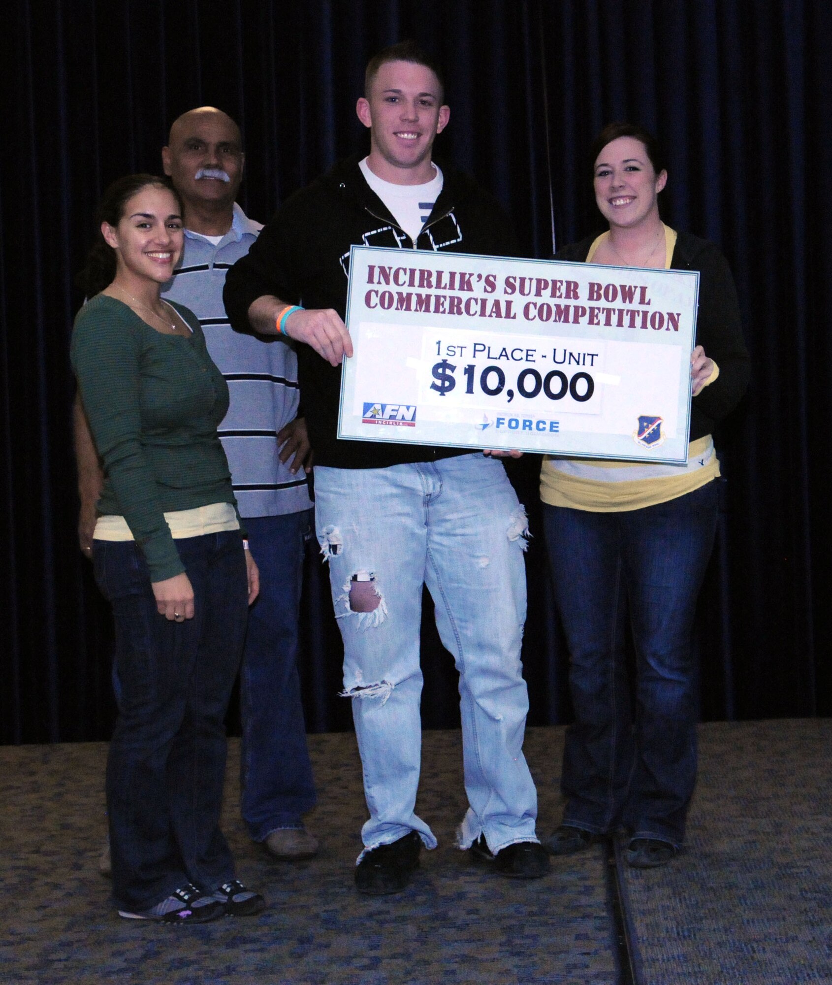 Senior Airmen Michael Jaeger and Jennifer Jolly, of the 39th Operations Squadron, pose with their $10,000 first-place prize at the finale of the Incirlik Super Bowl commercial contest, Feb. 7, 2011, at the consolidated club at Incirlik Air Base Turkey. The event was held in conjunction with the Super Bowl XLV screening event Feb. 6-7, and attendees had the opportunity to view and vote for their favorite locally-produced commercial. The second- and third-place winners received $6,000 and $4,000 respectively. The prize money is to be used for quality-of-life programs within the units.  Also pictured is 1st Lt. Gina McKeen, the 39th Air Base Wing public affairs chief, and Jorge Rodriguez, the consolidated club manager. (U.S. Air Force photo by Master Sgt. James Law/Released)