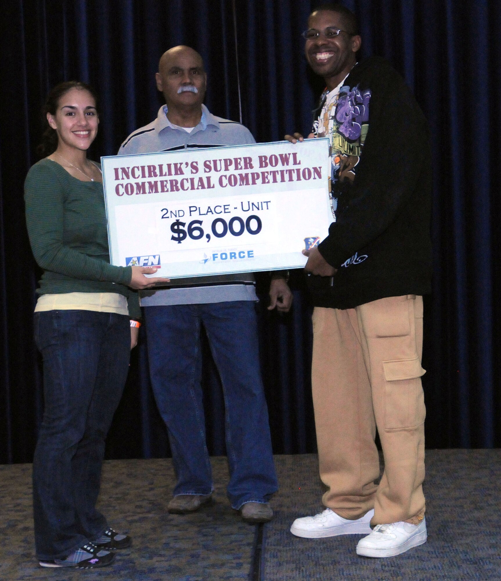 1st Lt. Gina McKeen, the 39th Air Base Wing public affairs chief, and Jorge Rodriguez, the consolidated club manager, present the $6,000 second-place prize to Airman 1st Class Jonathan Wooden, from the 39th Communication Squadron, at the finale of the Incirlik Super Bowl commercial contest Feb. 7, 2011, at the consolidated club on Incirlik Air Base, Turkey. The event was held in conjunction with the Super Bowl XLV screening event Feb. 6-7, and attendees had the opportunity to view and vote for their favorite locally-produced commercial. The first- and third-place winners received $10,000 and $4,000 respectively. The prize money is to be used for quality-of-life programs within the units. (U.S. Air Force photo by Master Sgt. James Law/Released)
