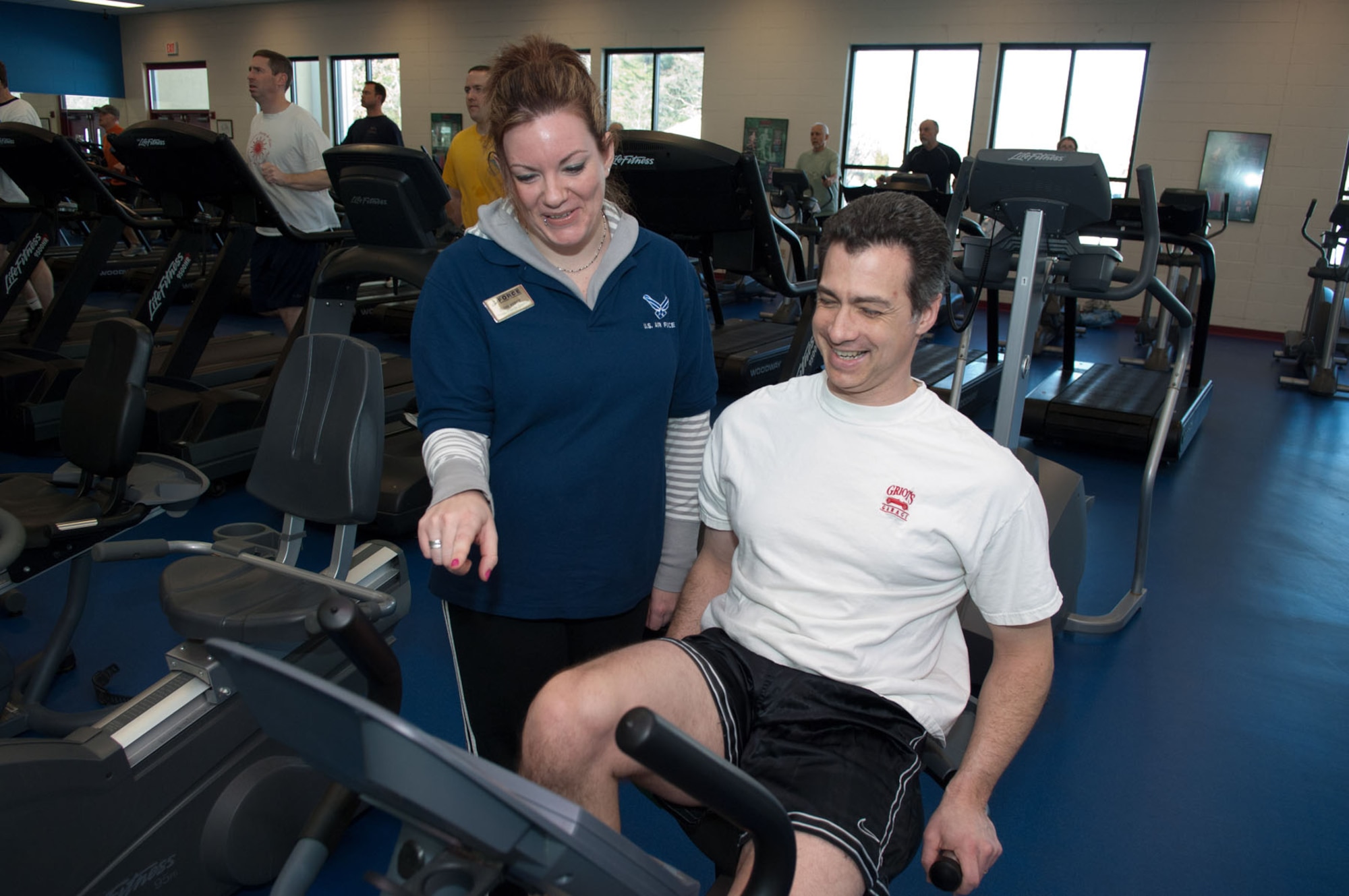 HANSCOM AIR FORCE BASE, Mass. – Olivia Kuntz (left), the Fitness Center’s fitness programs director, gives instructions on the bike to Pete McDonough on Feb. 16. Base personnel can schedule an orientation with Ms. Kuntz or other Fitness Center staff to learn more about fitness equipment, classes or services. (U.S. Air Force photo by Rick Berry)