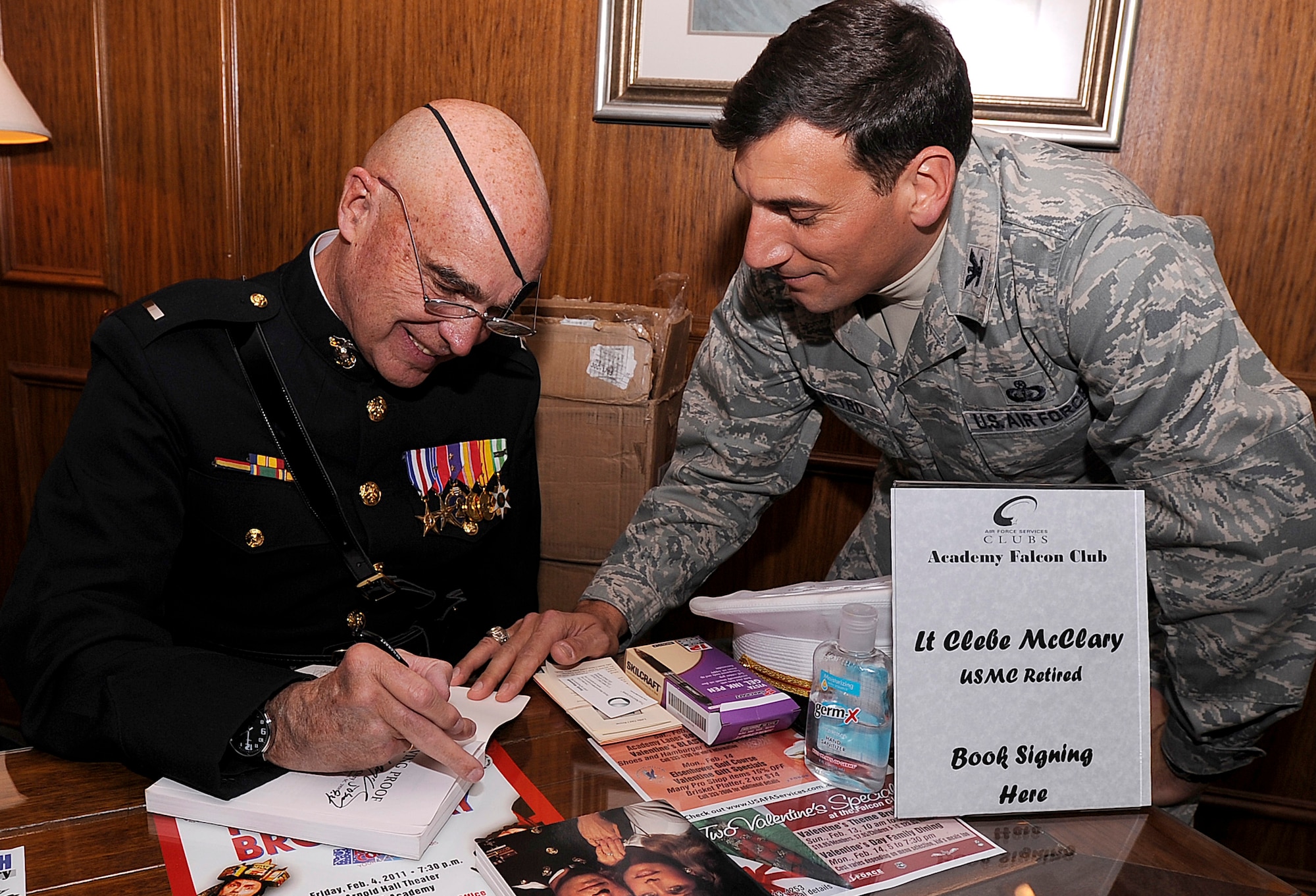 Retired Marine 1st Lt. Clebe McClary signs a copy of "Living Proof" for Col. Rick LoCastro in the Falcon Club after the Air Force Academy's National Prayer Luncheon Feb. 10, 2011. Lieutenant McClary was injured while serving in Vietnam. Colonel LoCastro is the 10th Air Base Wing commander. (U.S. Air Force photo/Mike Kaplan)