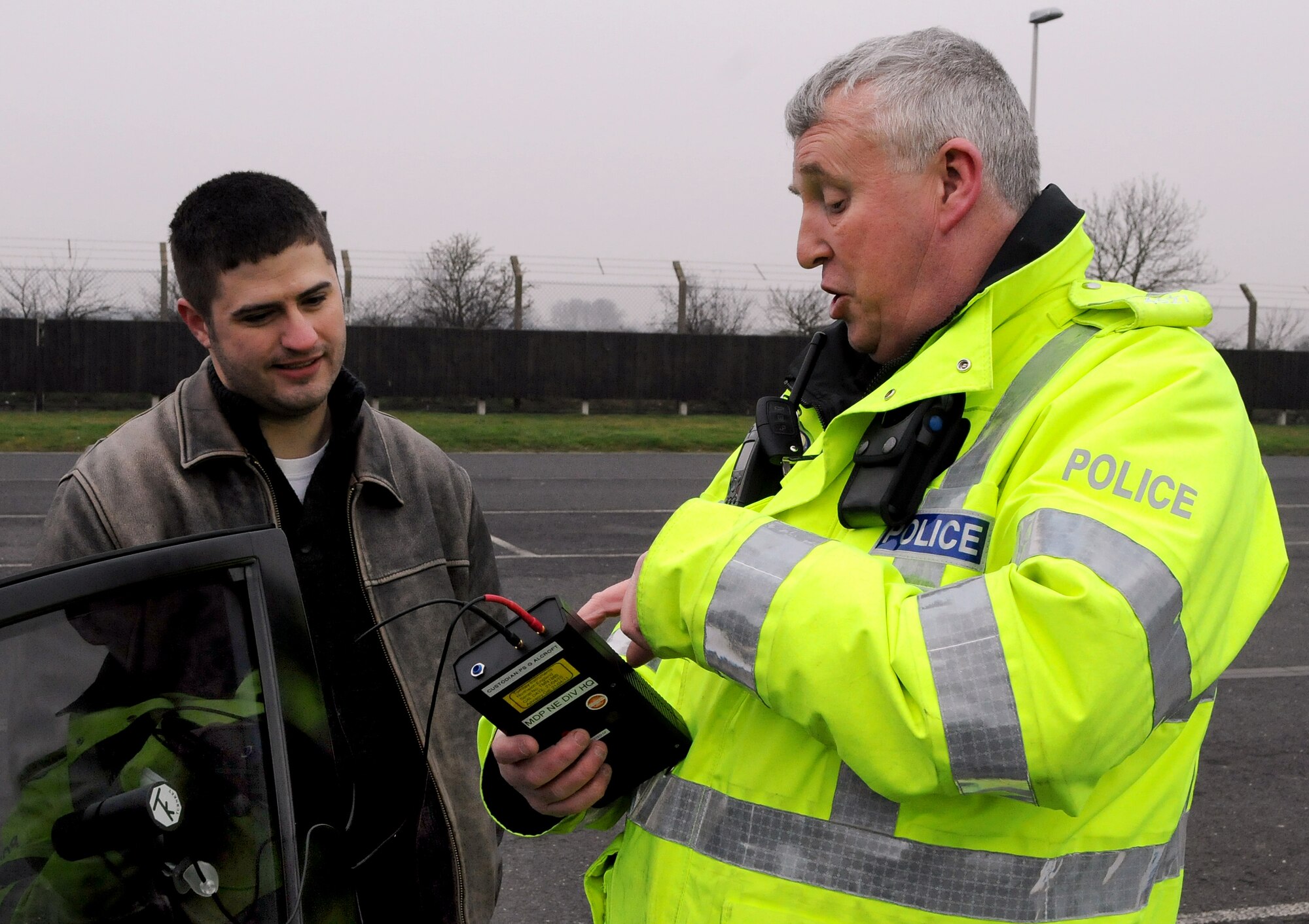 RAF MILDENHALL, England -- Police Constable Paul Glover, Ministry of Defence Police RAF Mildenhall, uses a photoptic vehicle tint tester to show David Hodge, Stars and Stripes reporter and photographer, the visible light transmission through his vehicle driver-side window here Feb. 18, 2011.  United Kingdom law requires windshields to have a minimum light transmission of 75 percent and front-side windows 70 percent. Suffolk Police are carrying out a 30-day amnesty all over Suffolk and are offering free VLT tests. However, if stopped after March 9, 2011, vehicle-owners will be prosecuted. (U.S Air Force photo/Senior Airman Tabitha M. Lee)