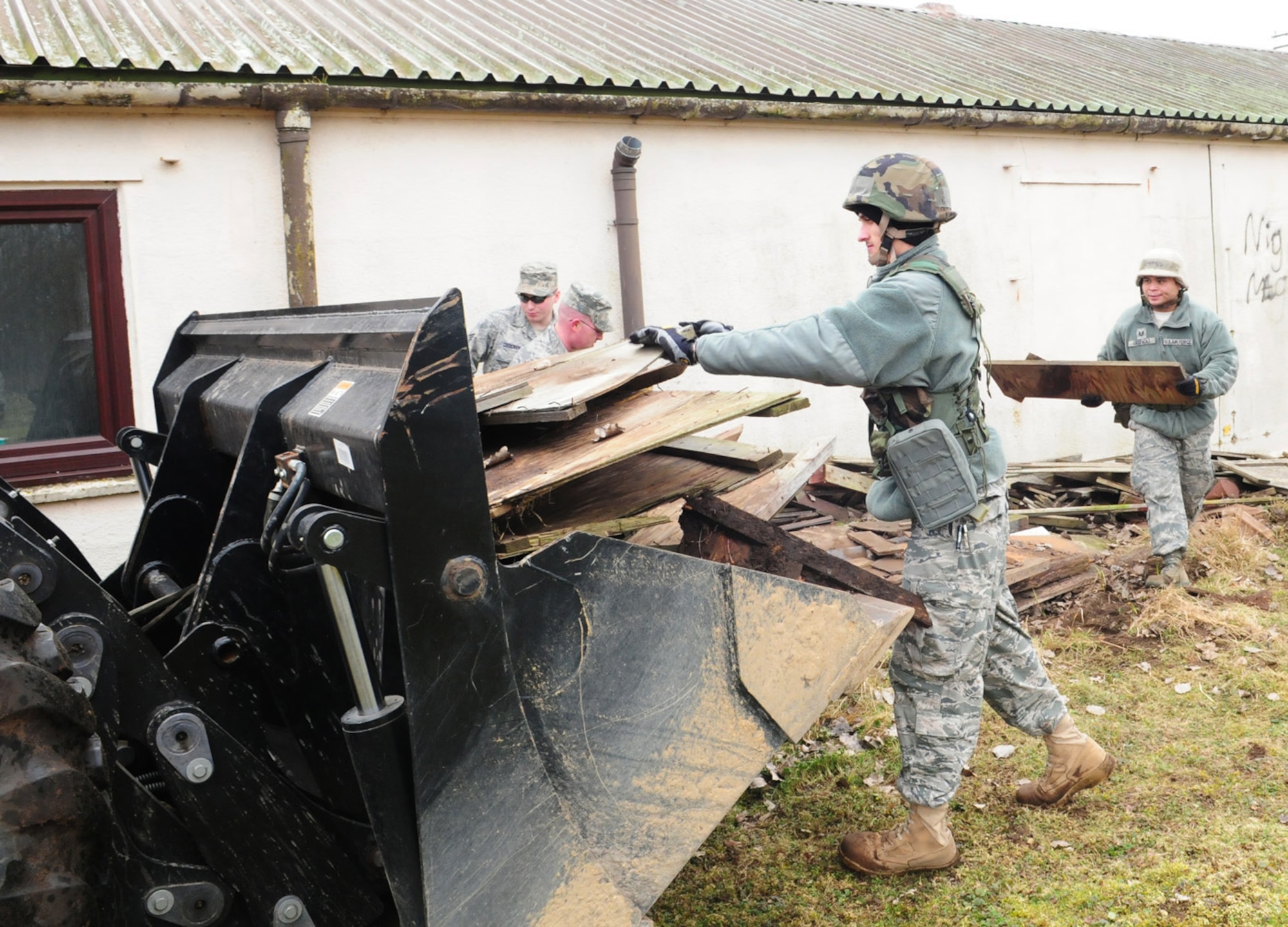 RAF MILDENHALL, England -- Members of the 100th Civil Engineer Squadron load wood and rubbish into the bucket of a digger at the "300 area" in Beck Row Feb. 17, 2011. The area, which has been leased to the Air Force, will be handed back to the Ministry of Defence Feb. 22. Personnel from the 100th CES electrical, structures, heating, ventilation and air conditioning, and horizontal shops performed the clean-up themselves, saving the base almost $9,000 in contracting fees. (U.S. Air Force photo/Karen Abeyasekere)