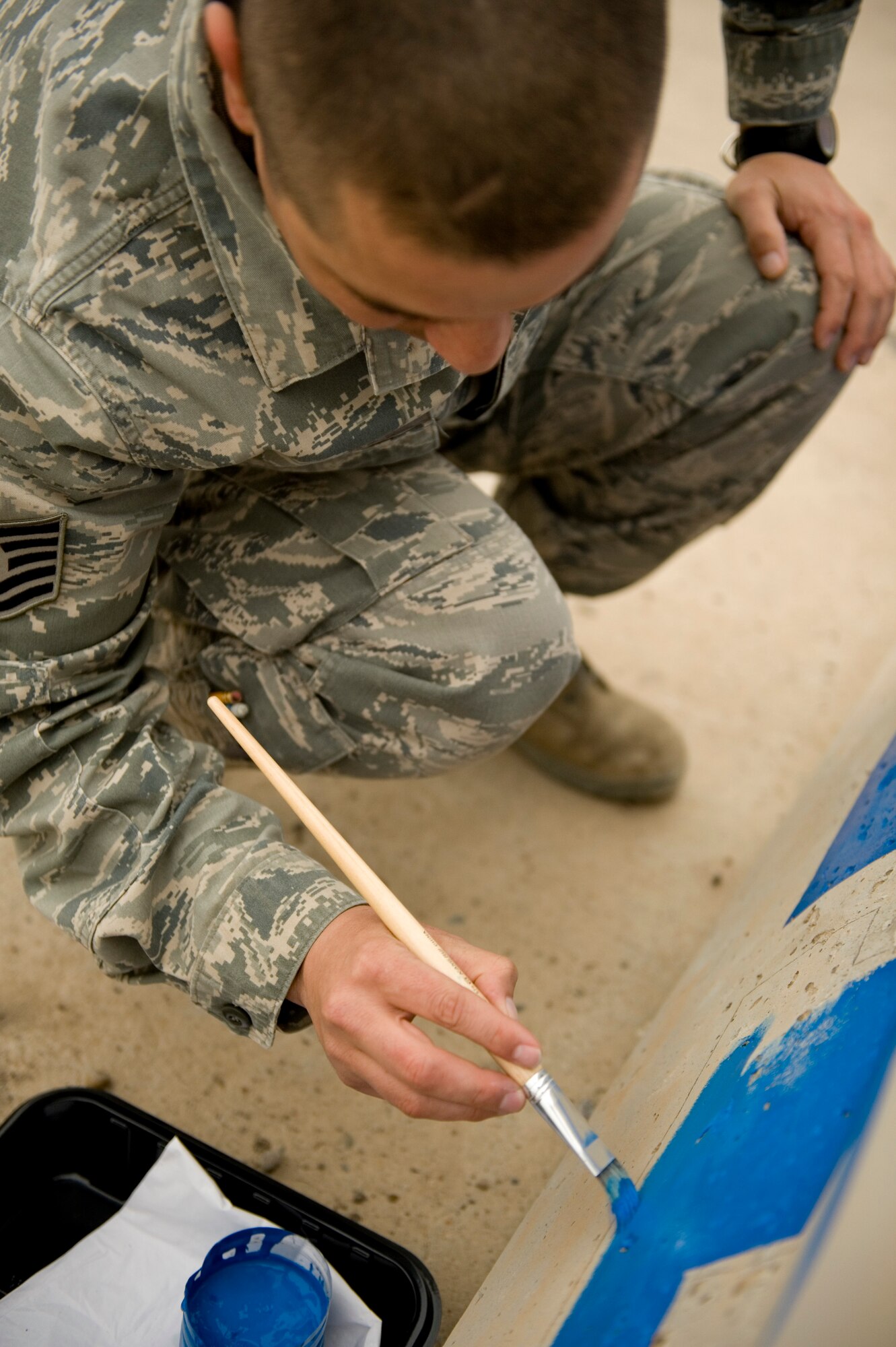 BAGHDAD - Tech. Sgt. Sergeant Lewis Isassi, 321st Expeditionary Mission Support Advisory Group advisor, paints a concrete barrier on the flightline at Sather Air Base Jan. 24. The mural improved the aesthetics of the area and promotes teamwork. Sergeant Isassi is originally from Kingsville, Texas, and is currently deployed from Spangdahlem Air Base, Germany. (U.S. Air Force photo by Staff Sgt. Levi Riendeau)