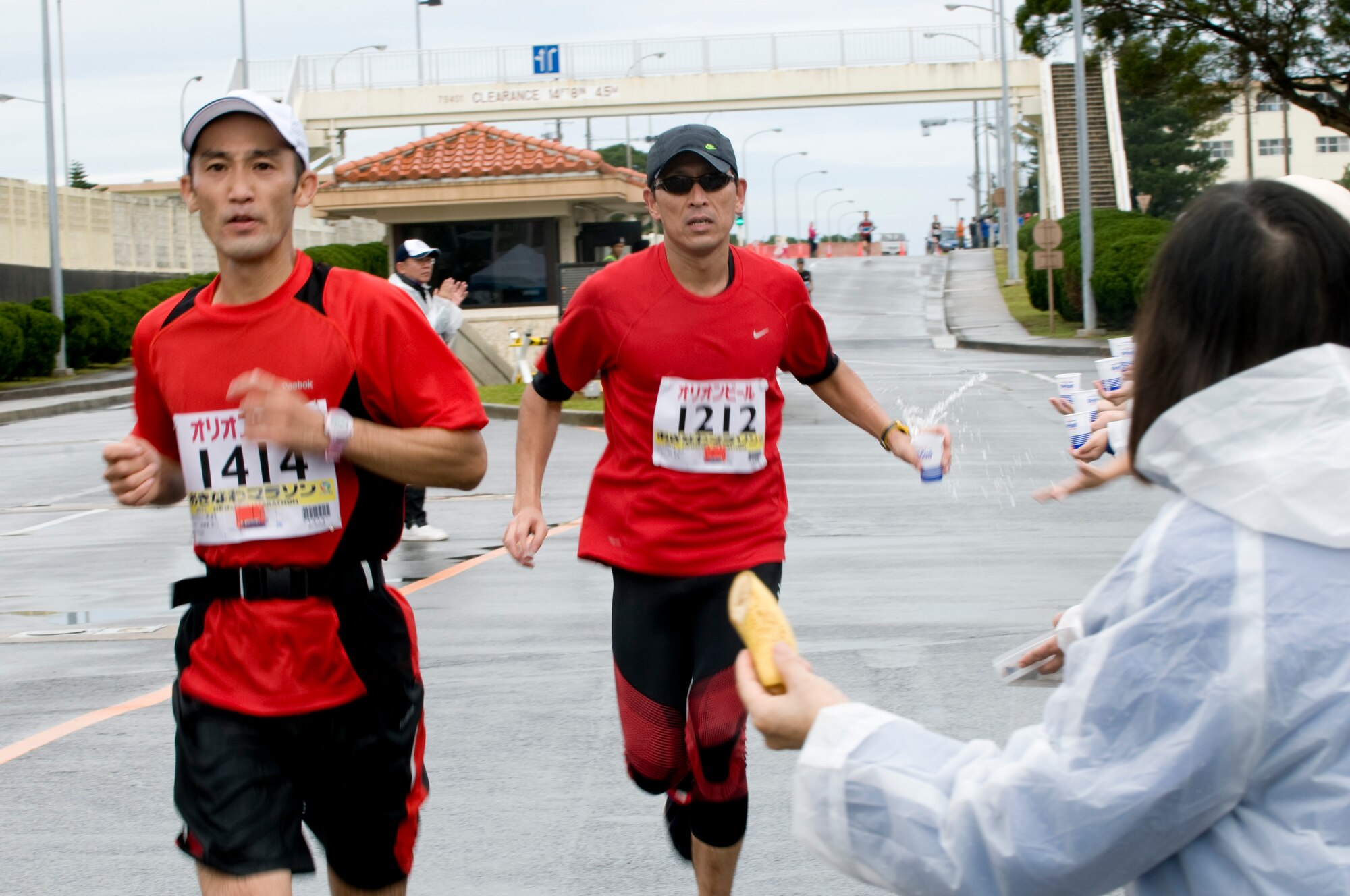 Runners participating in the 2011 Okinawa Marathon pass by a group of volunteers stationed along the marathon route through Kadena, while one runner accepts a cup of water, Feb. 20. Kadena service members and their families participated in the marathon by either running along the 26.2 mile route through the island’s cities, towns and villages, or by simply passing out water and fruit to the runners. (U.S. Air Force photo/ Brooke P. Beers)