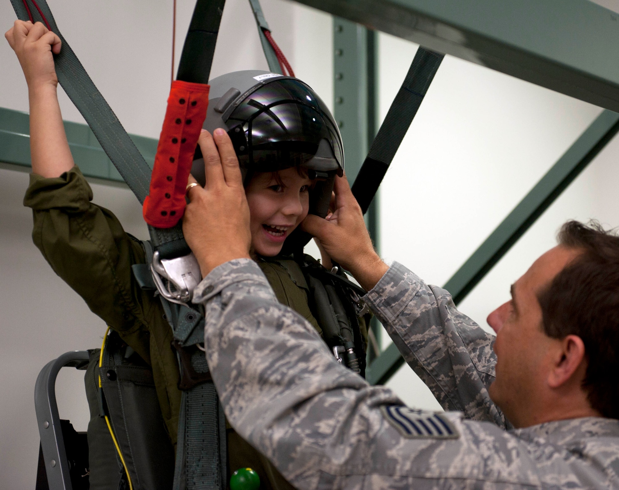 Zachary Tyrrell is given a flight helmet after being strapped into a parachute simulator by Tech. Sgt. Sherwood Brown, 15th Operations Support Squadron survival evasion resistance escape specialist Feb. 18 at the 535th Airlift Squadron during a "Pilot for a Day" tour on Joint Base Pearl Harbor Hickam, Hawaii. The goal of the program is to benefit children and their families in the local community who have catastrophic illnesses. Haley recently been declared cancer free after recovering from a cancerous brain tumor she was diagnosed with nearly two years ago. (U.S. Air Force photo/Staff Sgt. Nathan Allen)