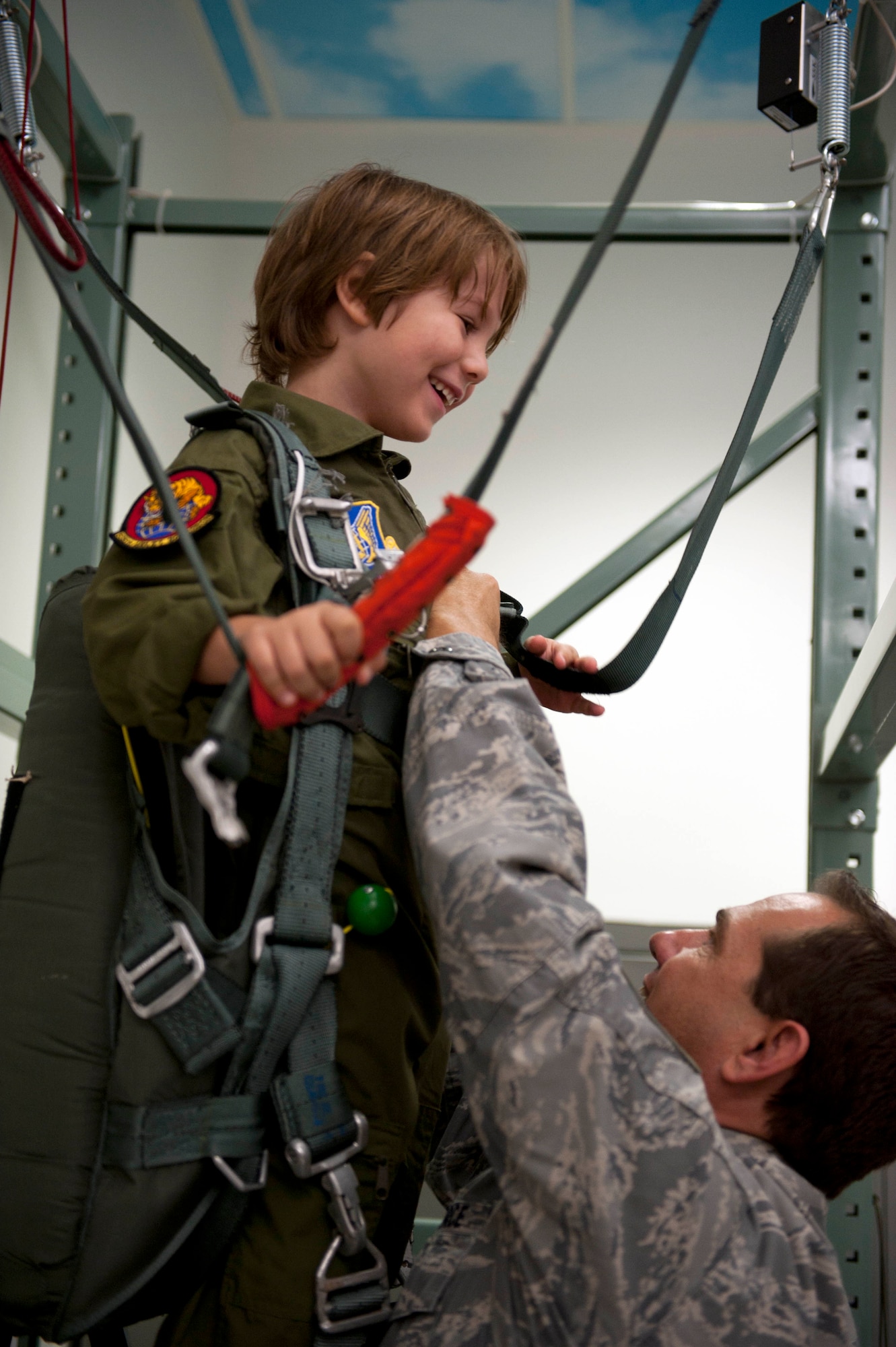 Zachary Tyrrell is strapped into a parachute simulator by Tech. Sgt. Sherwood Brown, 15th Operations Support Squadron survival evasion resistance escape specialist Feb. 18 at the 535th Airlift Squadron during a "Pilot for a Day" tour on Joint Base Pearl Harbor Hickam, Hawaii. The goal of the program is to benefit children and their families in the local community who have catastrophic illnesses. Haley recently been declared cancer free after recovering from a cancerous brain tumor she was diagnosed with nearly two years ago. (U.S. Air Force photo/Staff Sgt. Nathan Allen)