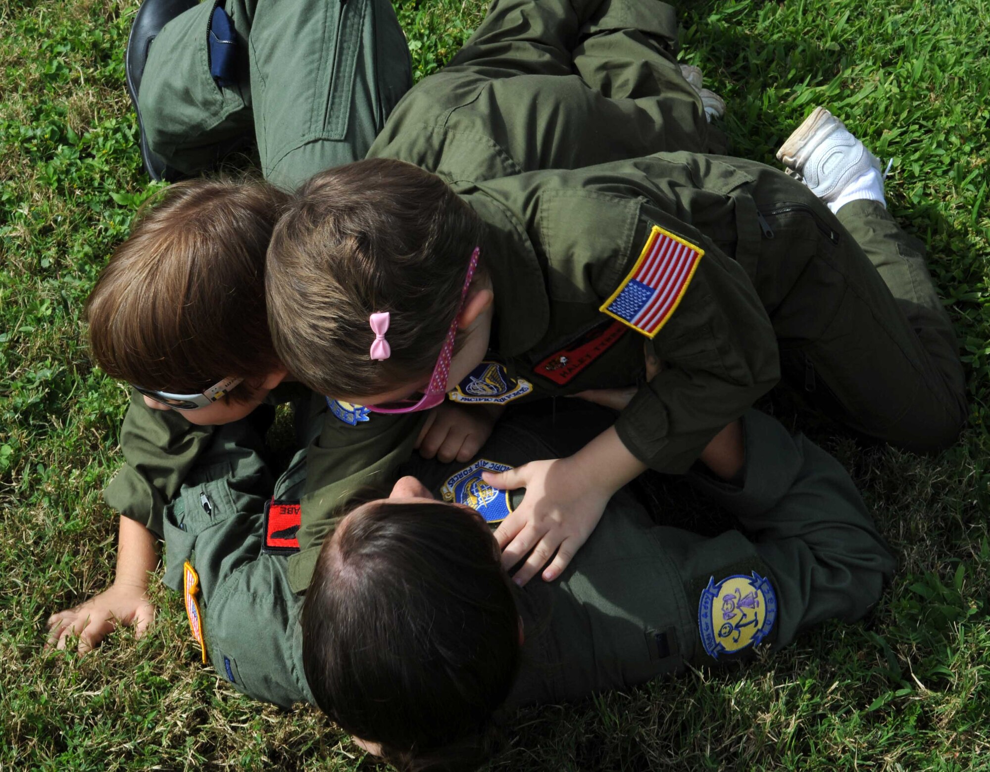 1st Lt. Audrey McCabe 535th Airlift Squadron C-17 Globemaster pilot and "Pilot for a Day" program "wingman," wrestles with Zachary Tyrell (left) and his sister Haley before watching a military working dog demonstration Feb. 18 at the kennels during a "Pilot for a Day" tour on Joint Base Pearl Harbor Hickam, Hawaii. The goal of the program is to benefit children and their families in the local community who have catastrophic illnesses. Haley recently been declared cancer free after recovering from a cancerous brain tumor she was diagnosed with nearly two years ago. (U.S. Air Force photo/Staff Sgt. Nathan Allen)