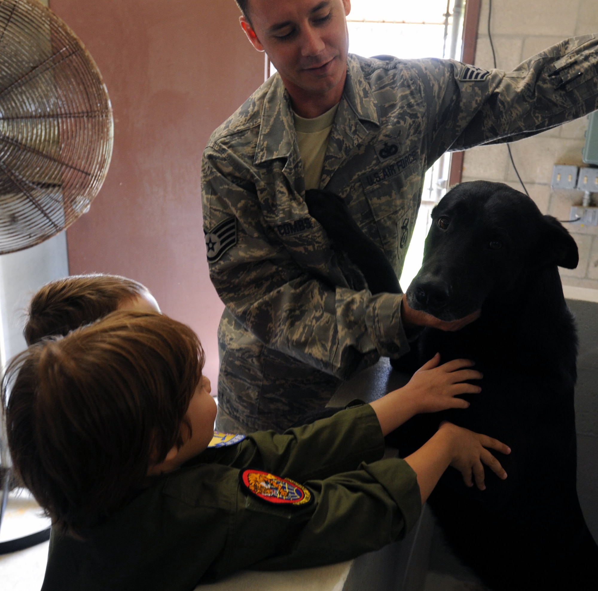 Zachary Tyrrell (front), his sister Haley, and Staff Sgt. Nathan Combs, 647th Security Forces Squadron military dog handler, pet "Aron" Feb. 18 at the kennels during a "Pilot for a Day" tour on Joint Base Pearl Harbor Hickam, Hawaii. The goal of the program is to benefit children and their families in the local community who have catastrophic illnesses. Haley recently been declared cancer free after recovering from a cancerous brain tumor she was diagnosed with nearly two years ago. (U.S. Air Force photo/Staff Sgt. Nathan Allen)