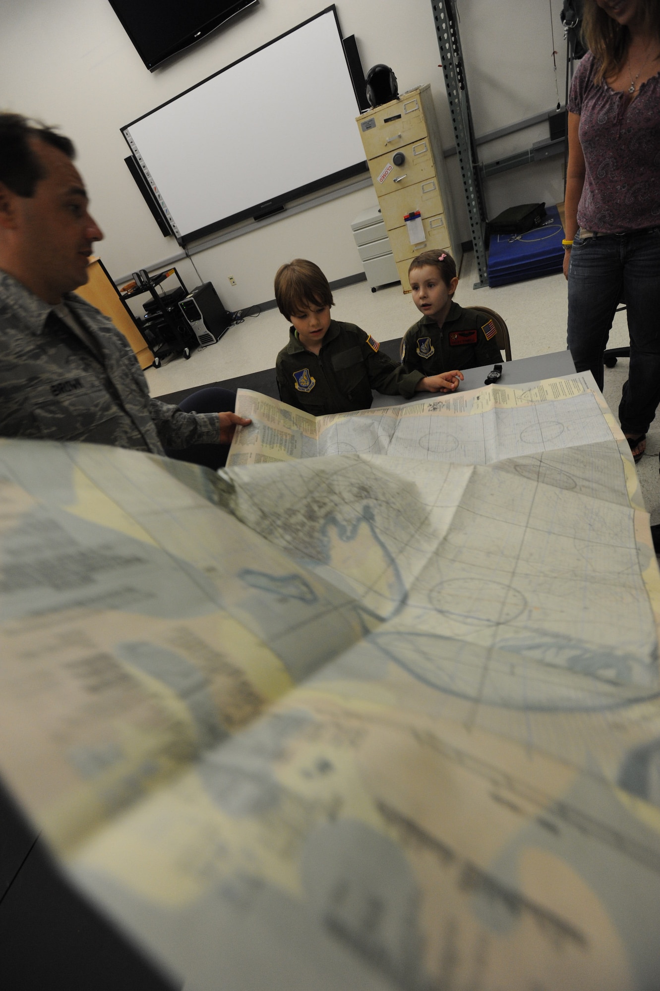 Tech. Sgt. Sherwood Brown, 15th Operations Support Squadron survival evasion resistance escape specialist shows a SERE map to Zachary (center) and Haley Tyrrell Feb. 18 at the 535th Airlift Squadron during a "Pilot for a Day" tour on Joint Base Pearl Harbor Hickam, Hawaii. The goal of the program is to benefit children and their families in the local community who have catastrophic illnesses. Haley recently been declared cancer free after recovering from a cancerous brain tumor she was diagnosed with nearly two years ago. (U.S. Air Force photo/Staff Sgt. Nathan Allen)