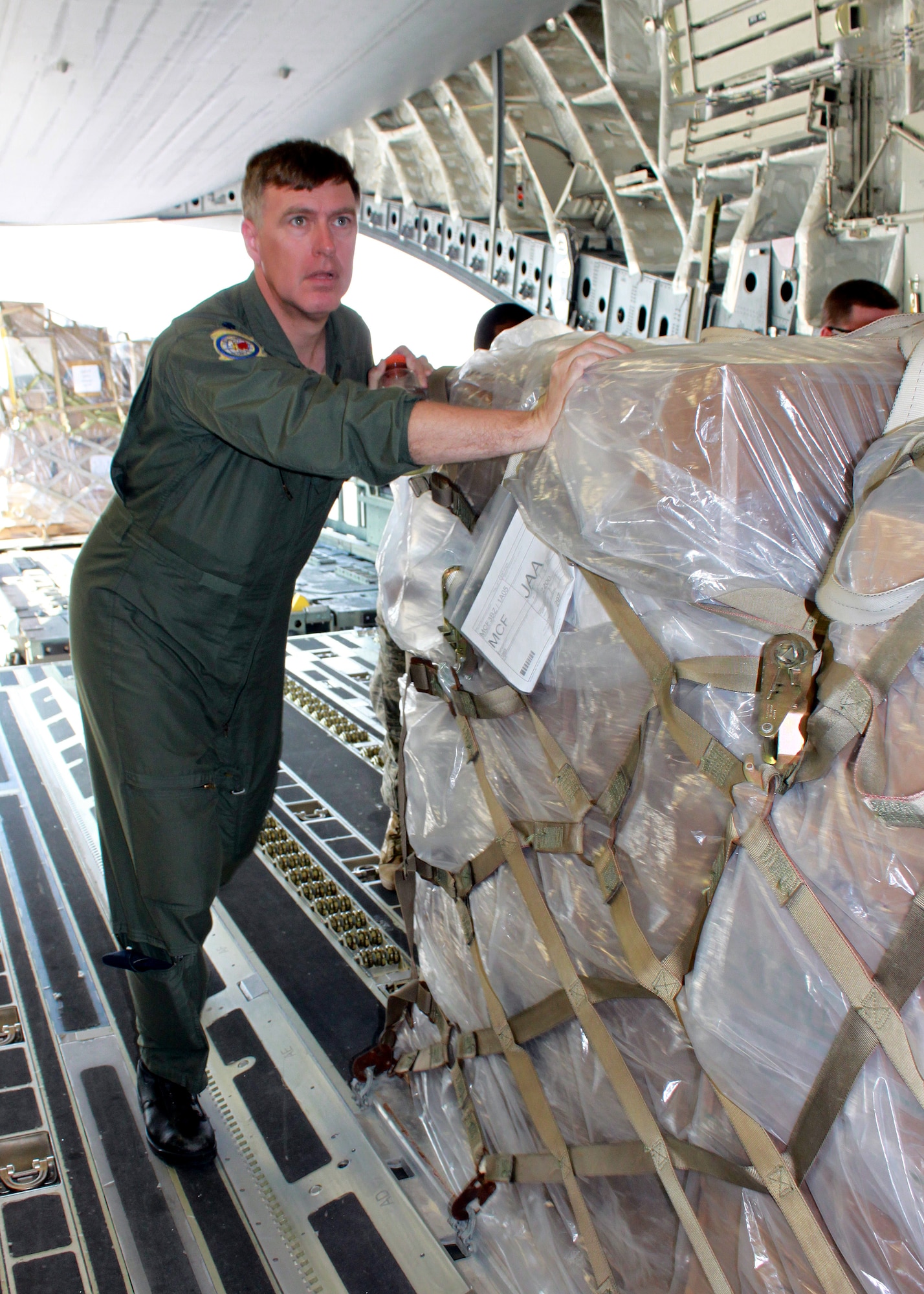 JOINT BASE MCGUIRE-DIX-LAKEHURST ? Lt. Col. Peter Debusmann, 732nd Airlift Squadron pilot, helps the aircrew push cargo palettes into place aboard the C-17 Globemaster III.  The C-17 aircrew accomplished training requirements with stops at three bases over the weekend to upload and download cargo under the Denton Program intended for delivery to Guyana and Afghanistan. The Denton Program authorizes the Department of Defense to transport donated assistance material, free of charge, on a Space Available basis and of no cost to the government other than the cost of transportation itself.