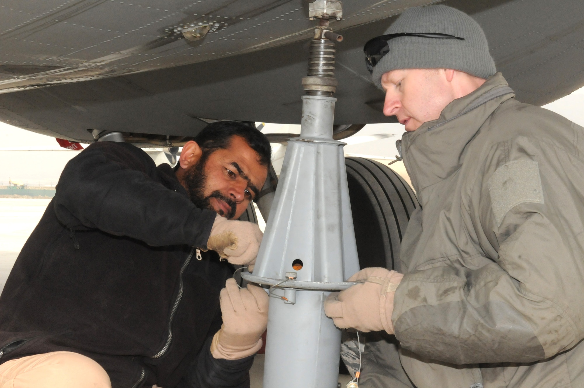 U.S. Air Force Master Sgt. Chris Neufeld, a NATO Air Training Command-Afghanistan C-27 loadmaster advisor with the 538th Air Expeditionary Advisory Squadron, helps an Afghan Air Force loadmaster-in-training apply a jack to a C-27 during an off-load mission at the Afghan Air Force Base in Kabul Feb. 21. (U.S. Navy photo by Mass Communications Specialist 2nd Class Vladimir Potapenko).