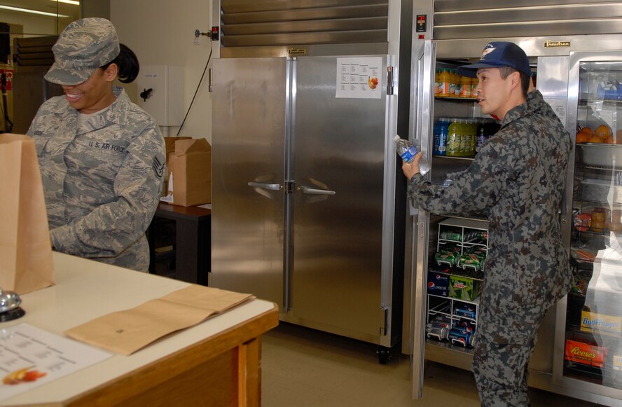 Staff Sgt. Naoki Yamane, a Japanese Air Self Defense Force food service specialist, assists Staff Sgt. Talandra Woods, non-commissioned officer in charge of the Johnson Dining Facility, with helping a customer. Sergeant Yamane came to Kadena to participate in an NCO exchange program that gave both Japanese and American Airmen insight into how their counterparts operate. (U.S. Air Force photo/ Airman 1st Class Tara A. Williamson)