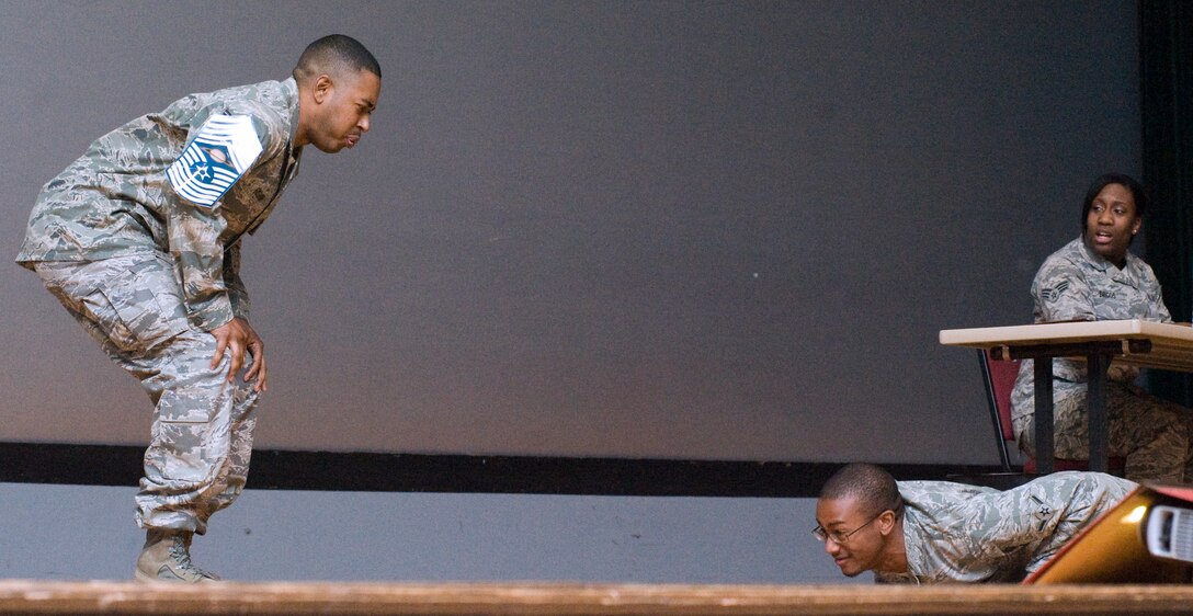 Staff Sgt. Donte Bishop, left, self proclaimed “Super NCO”, 11th Force Support Squadron manpower analyst, randomly orders Airman Jamel Brown, 11th Comptroller Squadron finance technician, to perform push ups as Senior Airman Felisha Briggs, 11 FSS customer service technician, observes in shock during a skit at the Base Theater Feb. 22. The Andrews members, better known as the ‘Andrews Players,’ are volunteer actors. The players depicted how Airmen could show resiliency in the midst of adverse conditions in the military life as well as in their personal lives. (U.S. Air Force photo/Bobby Jones)
