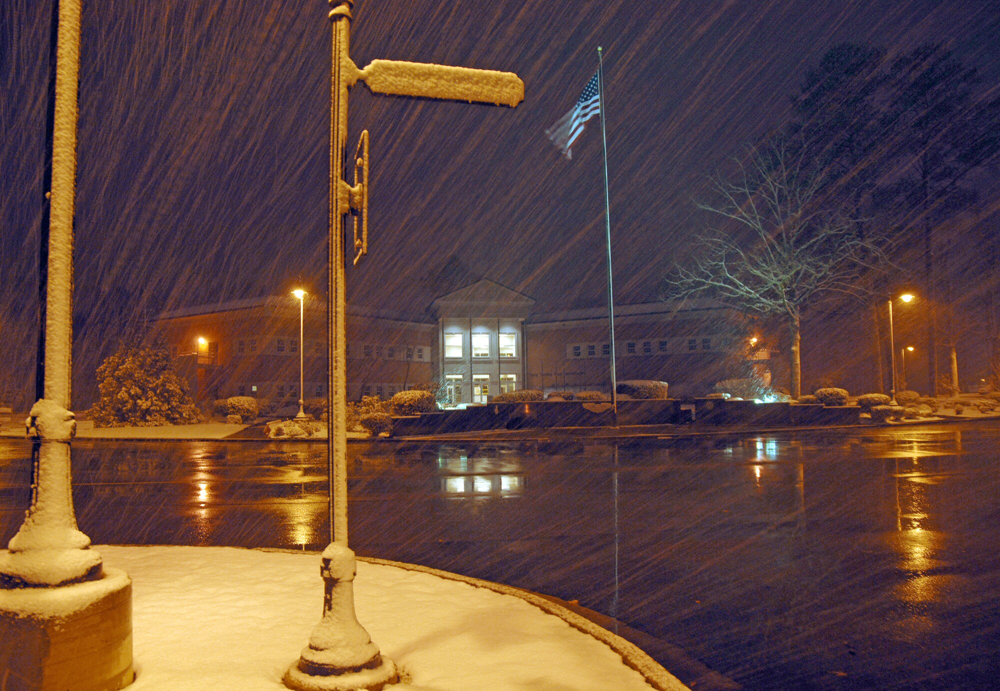 Snow falls across the front of the near complete 14th Flying Training Wing Headquarters Building here on Feb. 9, as the American Flag flies freely in the night sky. Nearly two inches of snow fell during the night providing children of the base a "Snow Day" and the rest of Team BLAZE a chilly work day.