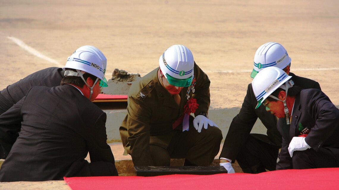 Col. David P. Olszowy, center, commanding officer, III Marine Expeditionary Force Headquarters Group, III MEF, places mortar around a cornerstone with other distinguished guests during a cornerstone burial ceremony at Okukubi Dam in the Central Training Area Feb. 26. The project has been in development for nearly 40 years and when complete, the dam will hold more than 7.6 million cubic meters of fresh water to be used to irrigate crops and protect land and property from flooding.