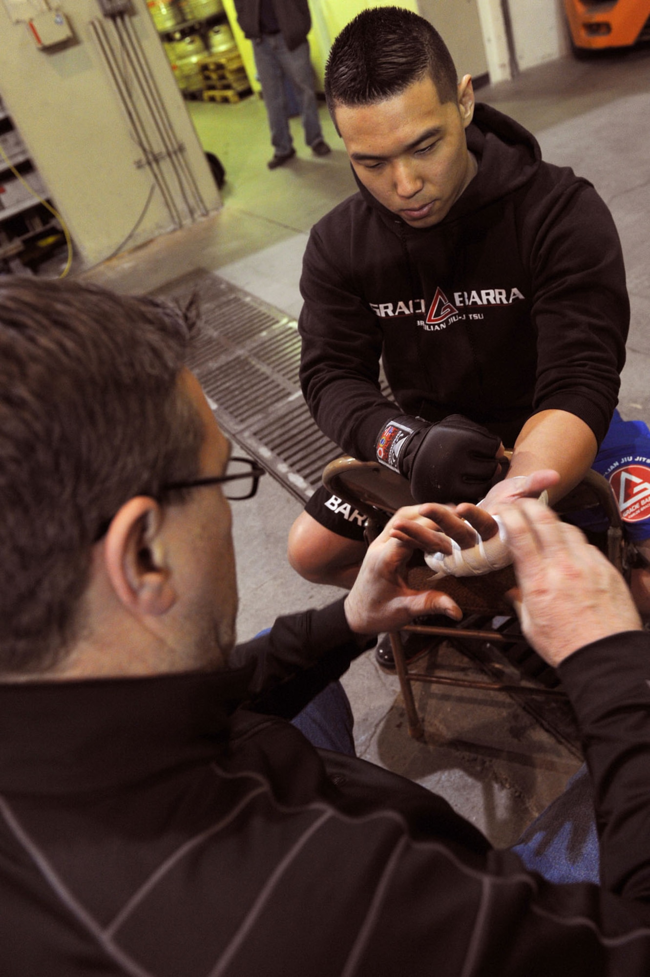 ANCHORAGE , Alaska -- Airman 1st Class Nojin “Ian” Park, 3rd Maintenance Operation Squadron, gets his fists taped by Jim Dooley, from the Gracie Barra gym, prior to his first Alaska Fighting Championship match at the Anchorage Sullivan Arena on February 17. Fighters wrap their hands to add extra protection while fighting. (U.S. Air Force Photo by Staff Sgt. Joshua Garcia)