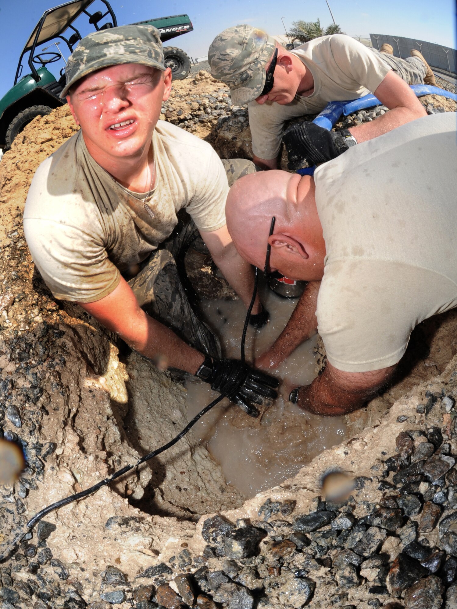 Staff Sgt. Joshua Witmer takes a splash of water to the face as he and Tech Sgt. George Burns try to fix the water main break, while Staff Sgt. Frank Murphy, 380 ECES, mans the vacuum near Windy's Feb. 7, 2011. All are assigned to the 380th Expeditionary Civil Engineer Squadron here.  Water main breaks are common as the ground randomly shifts, affecting pipes around it. Sergeant Witmer and Murphy are deployed from Andrews AFB, Md., while Sergeant Burns is from the 341st CES out of Malstrom AFB, Mont . (U.S. Air Force photo by Senior Airman Maynelinne De La Cruz)