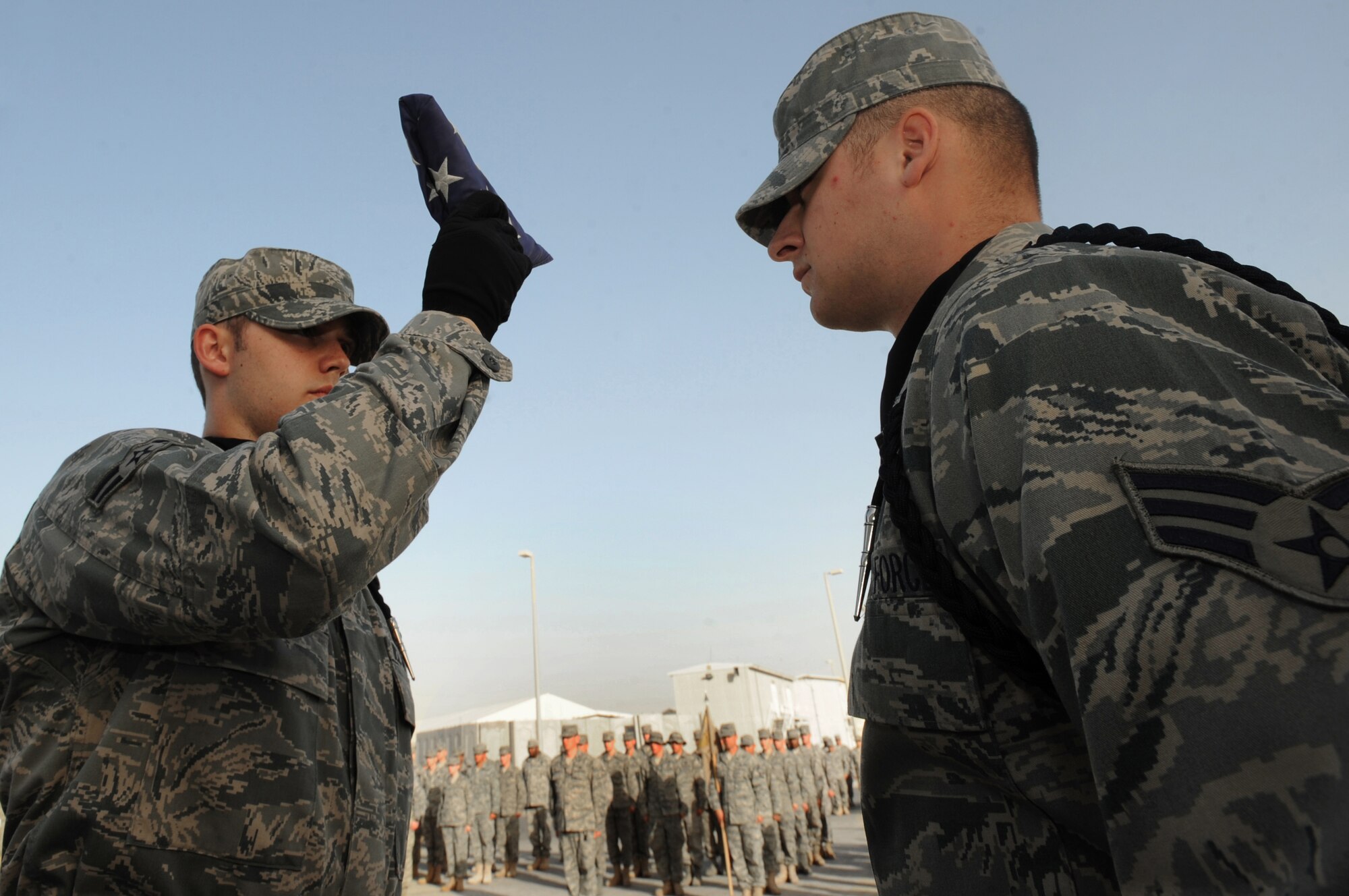 Airman 1st Class Alec Krabbe, 380th Expeditionary Communications Squadron, presents the American Flag while Senior Airman David Hunt, 380th Expeditionary Civil Engineer Squadron, waits to receive it on Feb. 5, 2011, in Southwest Asia. The retreat ceremony signals the end of the official duty day and serves as a ceremony to pay our respects to the flag. Airman Krabbe is deployed from the 633rd CS, Langley AFB, Va.; Airman Hunt is deployed from the 27th Special Operations CES, Cannon AFB, New Mexico. (U.S. Air Force photo by Senior Airman Maynelinne De La Cruz)
