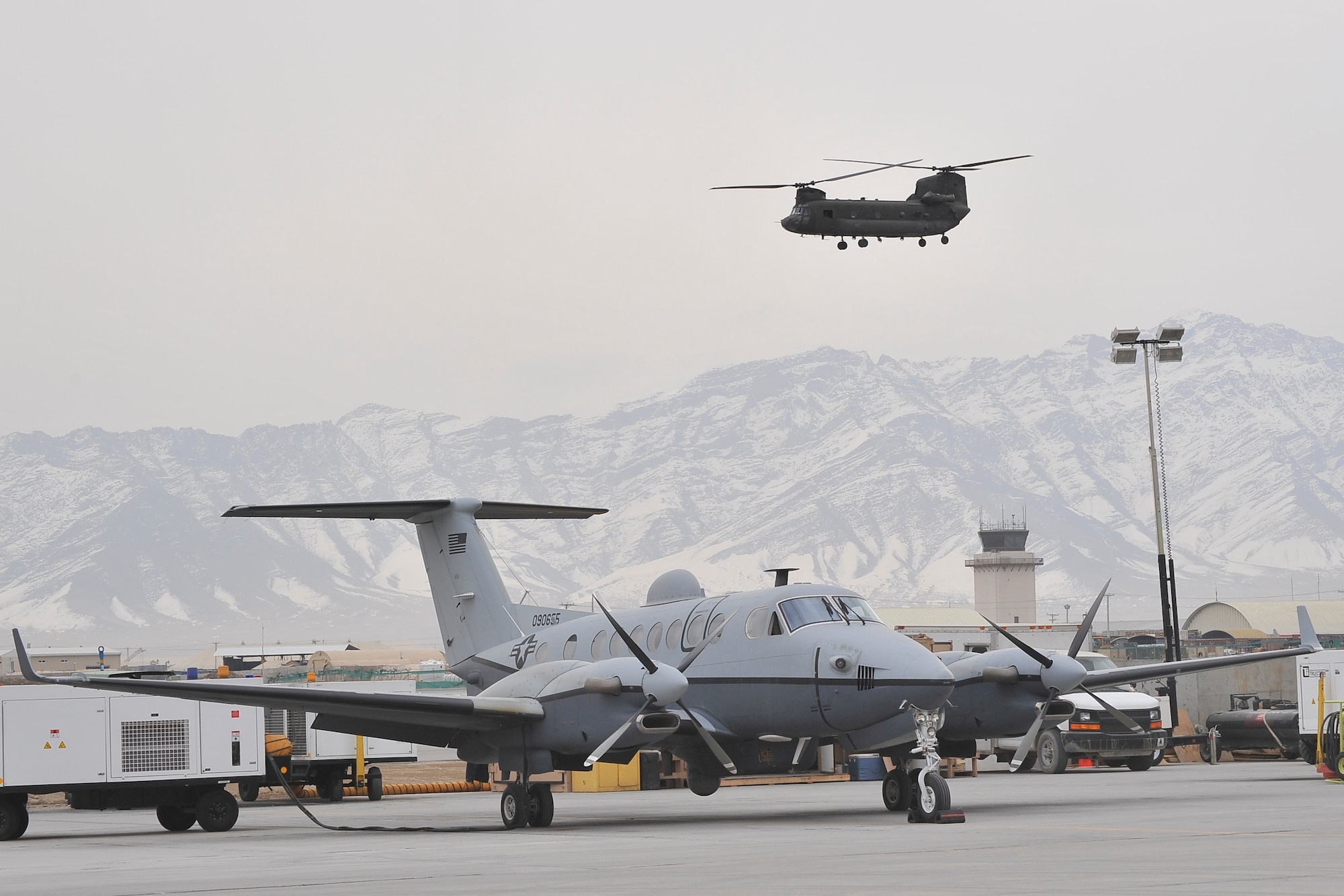 A MC-12 Liberty sits on the apron at Bagram Airfield, Afghanistan, while a CH-47 Chinook takes off.  The MC-12 provides intelligence, surveillance and reconnaissance support directly to ground forces. 