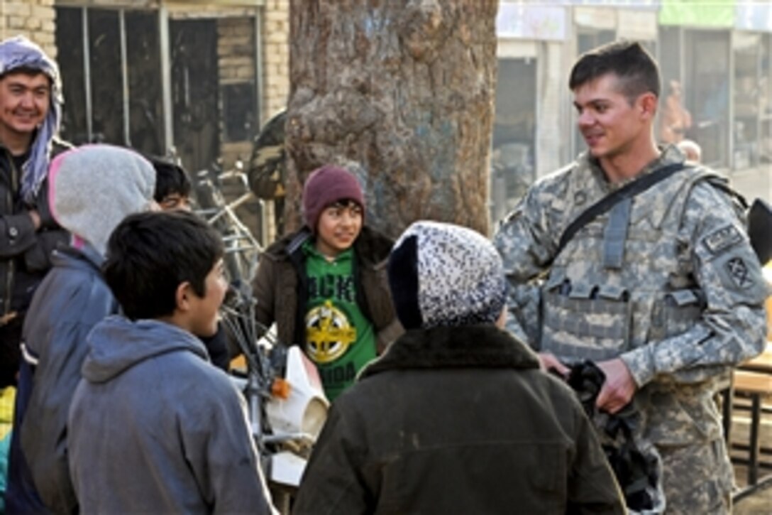 U.S. Army 1st Lt. Pierce Pettis talks to village children as U.S. and Afghan soldiers load school desks onto their vehicles near Bagram Airfield, Afghanistan, Dec. 30, 2010. The U.S. troops are assigned to the 87th Combat Sustainment Support Battalion, 101st Sustainment Brigade. The new desks are part of the first major project between the battalion and the Afghan forces.