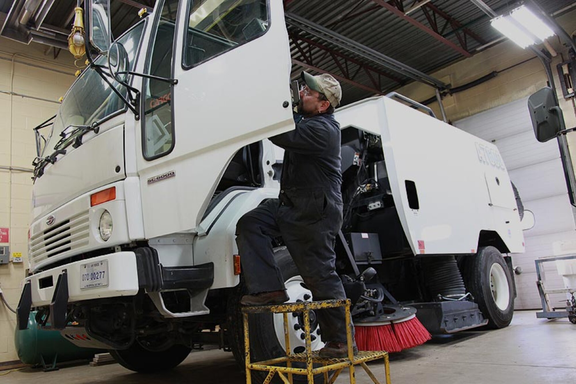 Bob Haines, a civilian mechanic employed by the contractor Maytag Aircraft, works on one of the two base sweeper trucks, Jan. 4.