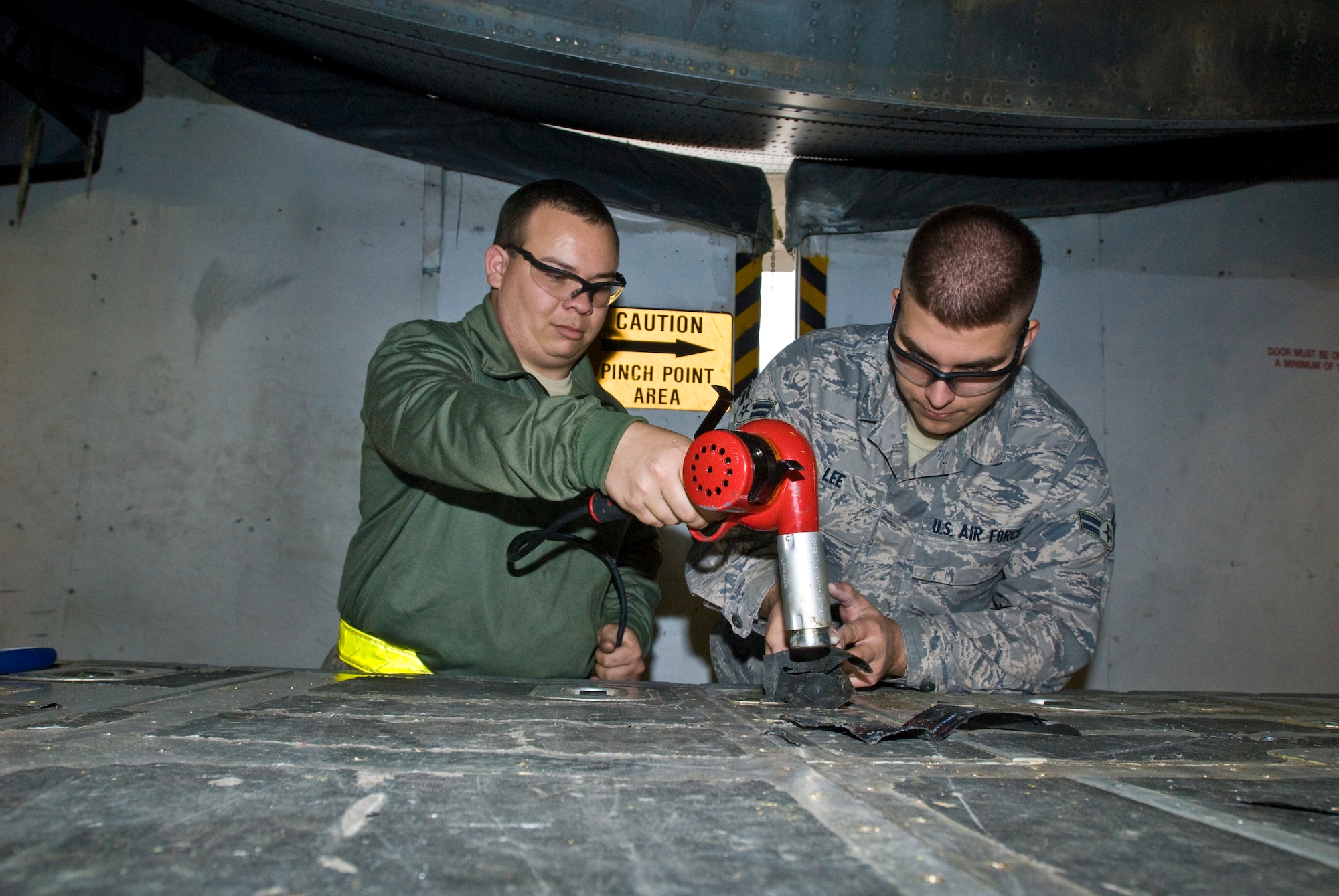 Senior Airman Daniel Maguire (left), a 19th Equipment Maintenance Squadron aircraft structural maintenance journeyman, and Airman 1st Class David Lee, a 19th EMS crew chief, work together to remove anti-skid from a C-130 aircraft’s cargo floors Wednesday. Refurbishing aircraft is not an actual Air Force specialty code but a special program. (U.S. Air Force photo by Staff Sgt. Nestor Cruz)